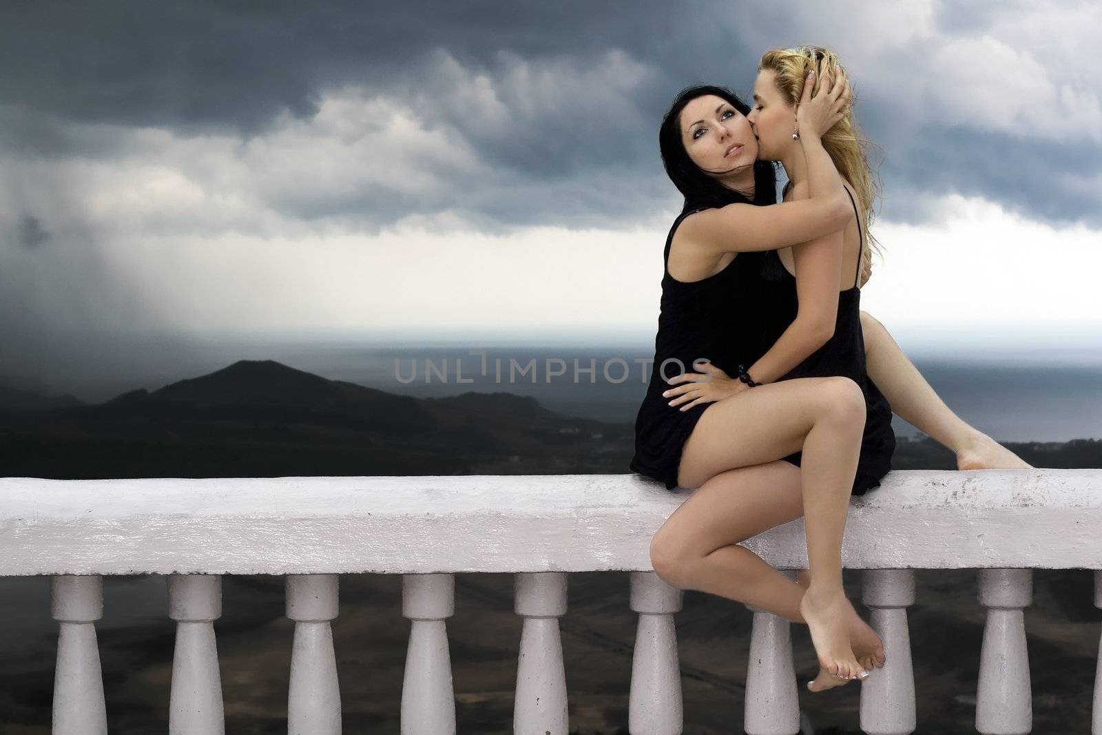 Two pretty embracing girls sit on a handrail