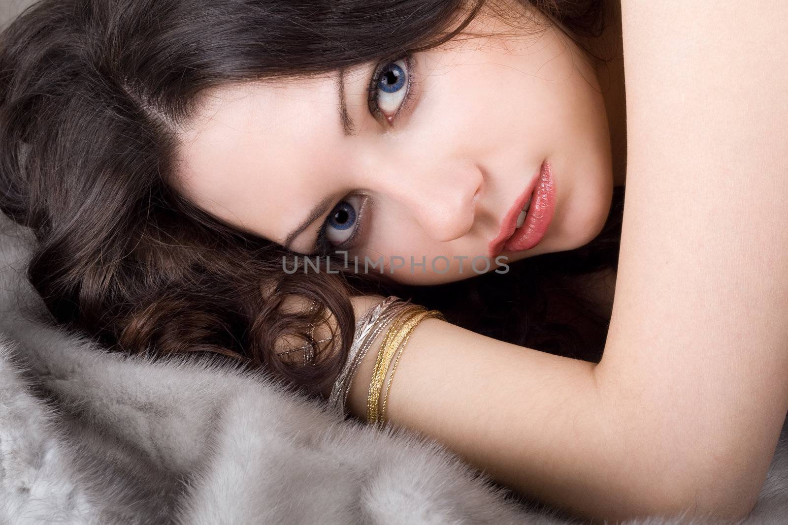 Lovely young woman lying on grey fur coat