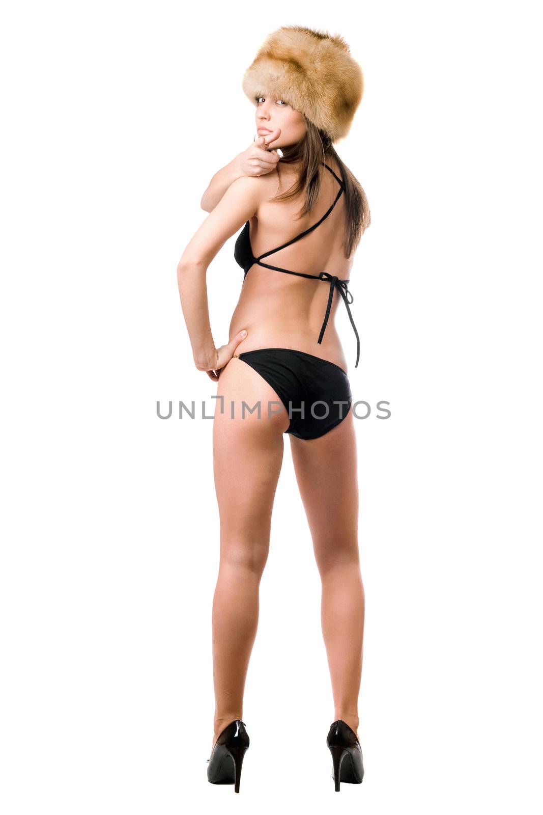 Sexy brunette in black swimsuit and fur-cap standing with her back. Isolated
