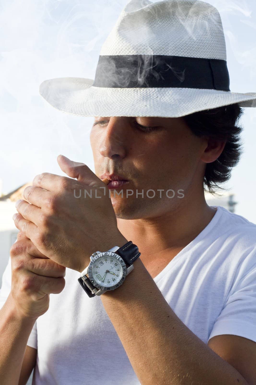 View of a handsome man with white shirt and hat on a urban city lighting a cigarette.
