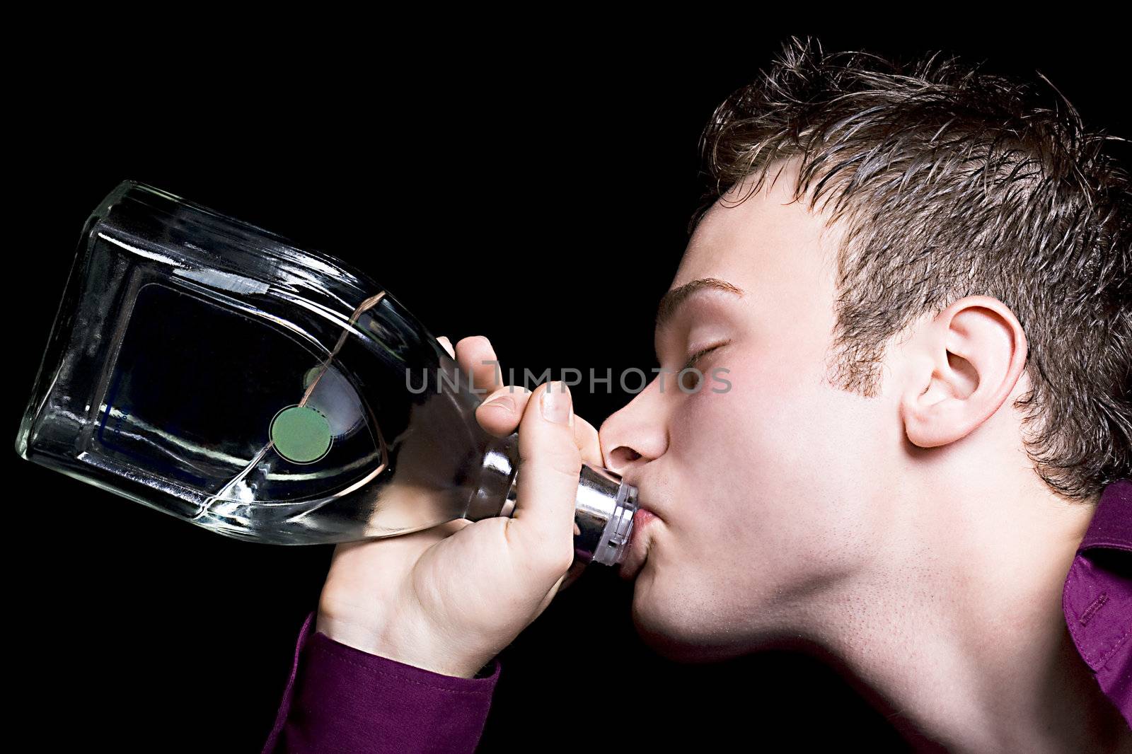 The young man drinks vodka from a bottle. Isolated on black by acidgrey