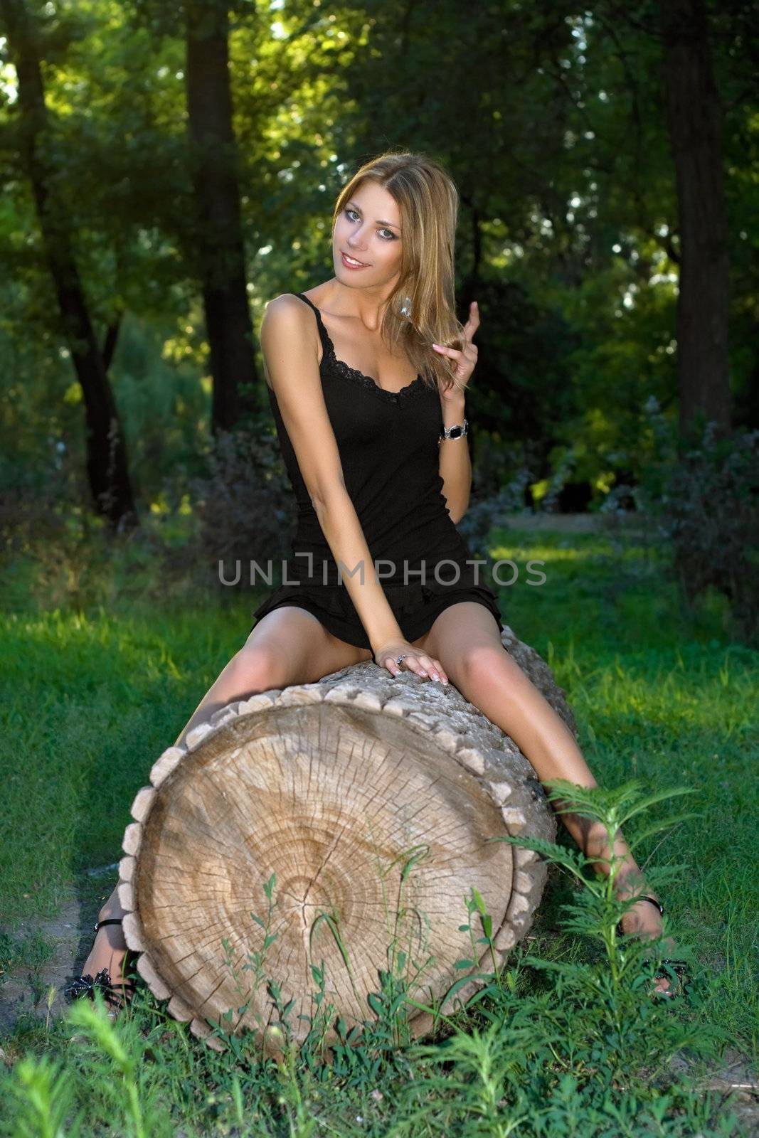 Pretty young blonde sitting on a felled trunk tree