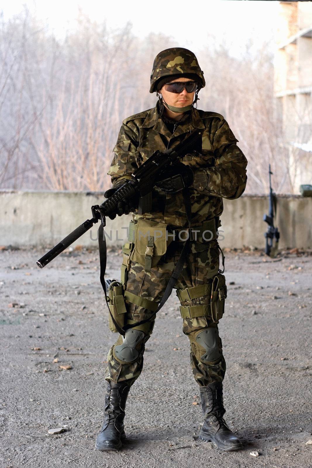 Military guy holding a gun in front of neglected building