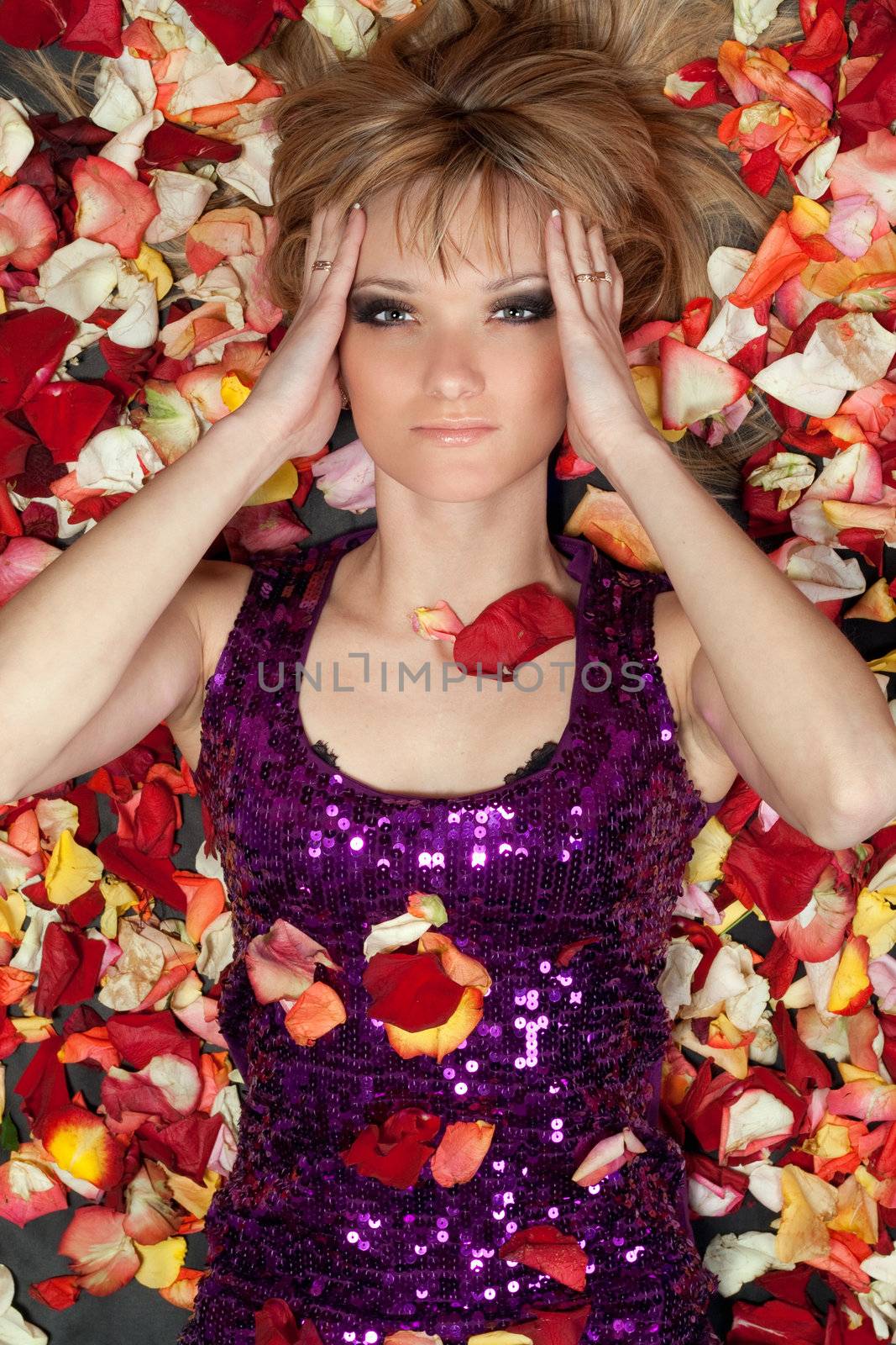 Portrait of lovely young blonde lying in rose petals