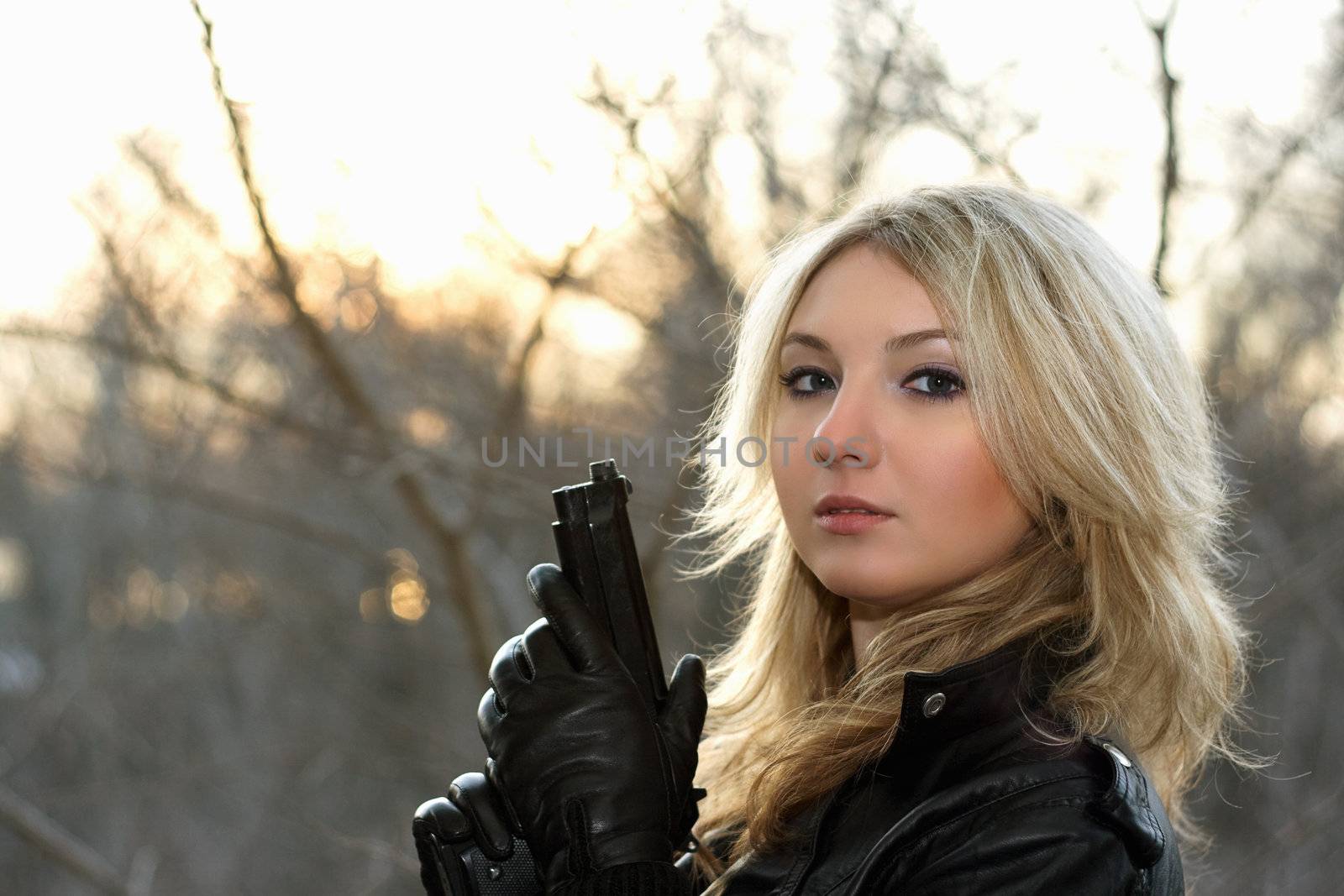 Blonde young woman with a gun at the sunset