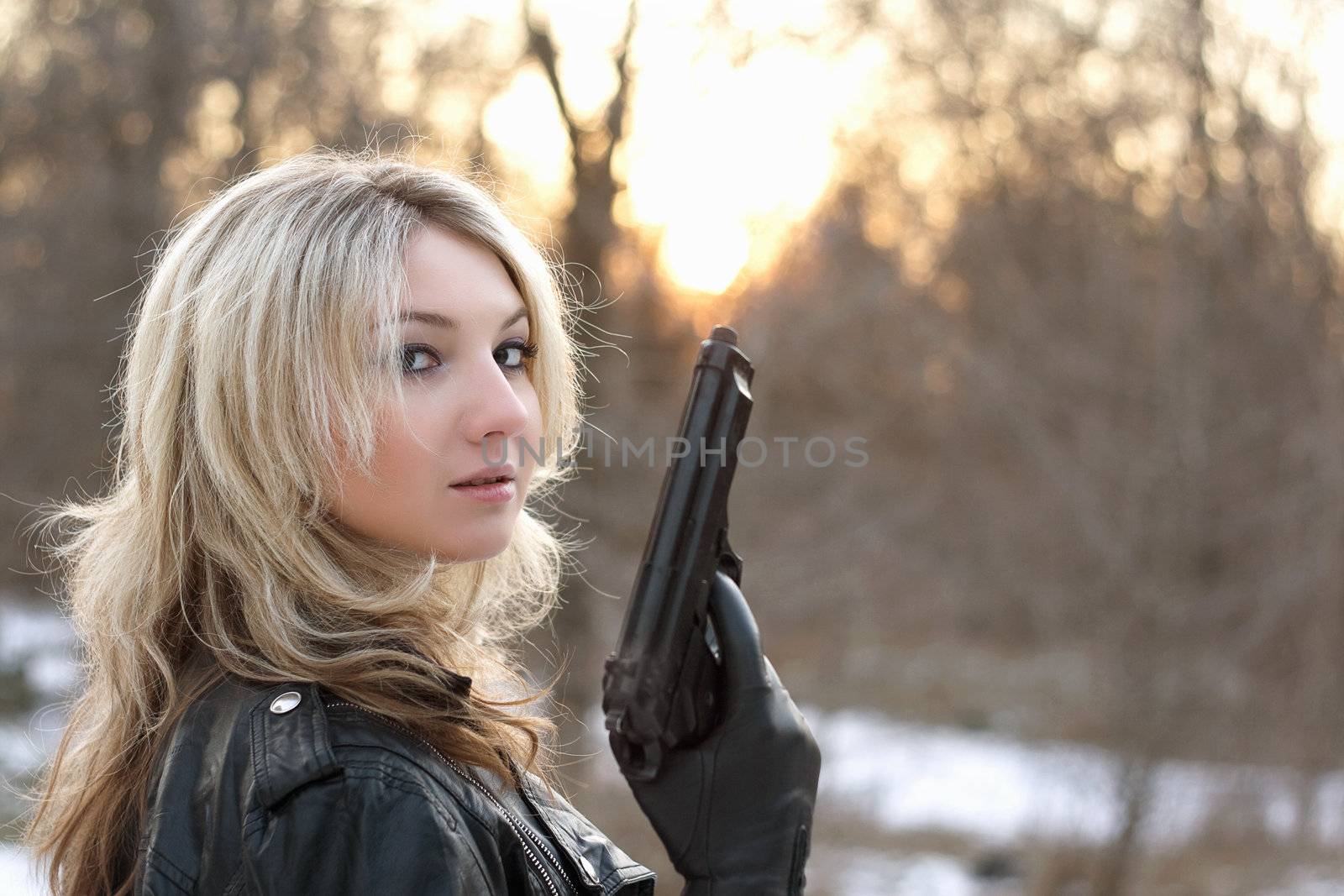 Provocative young woman holding a gun in winter forest