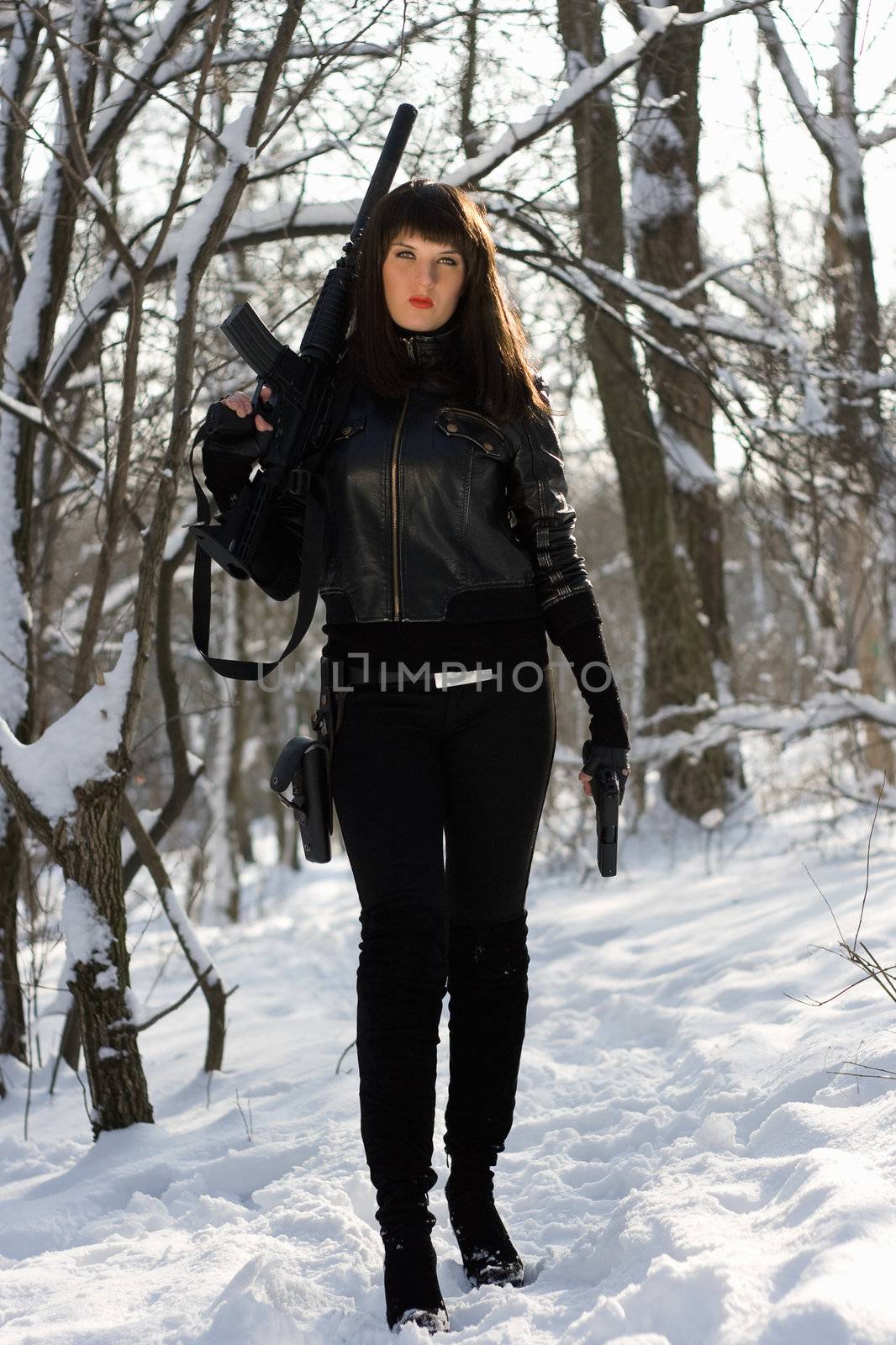Beautiful young woman with a rifle and pistol in winter forest