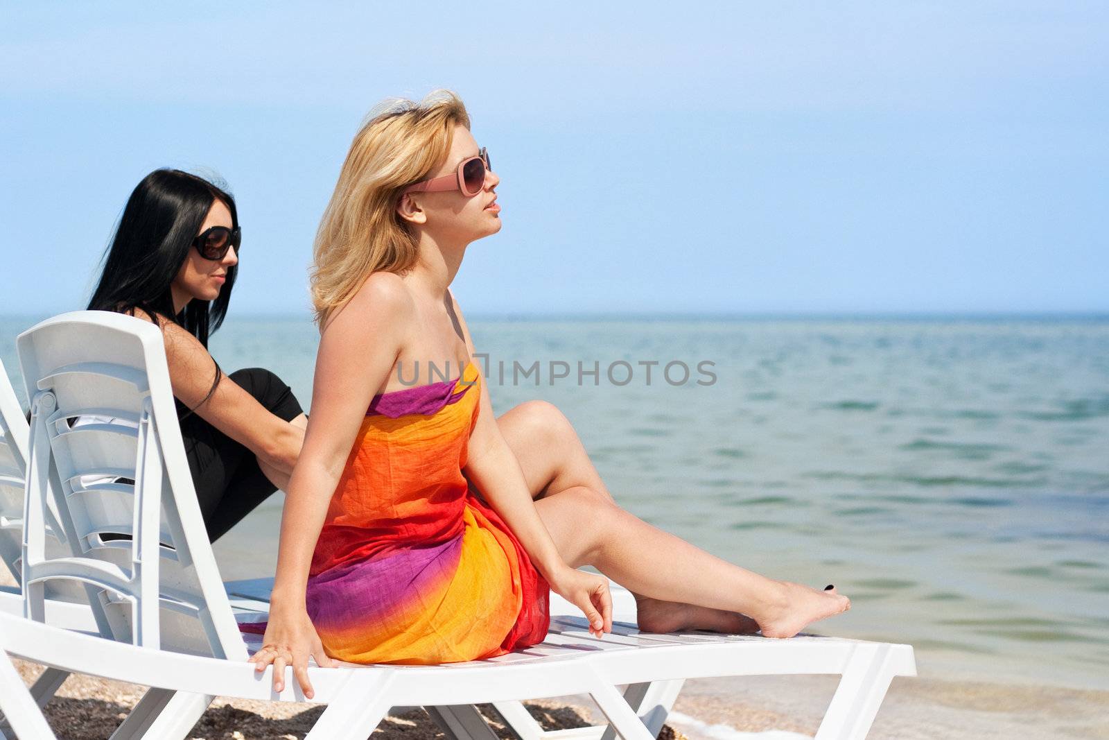 Two beautiful young women sitting on a sunbeds. Focus on blonde