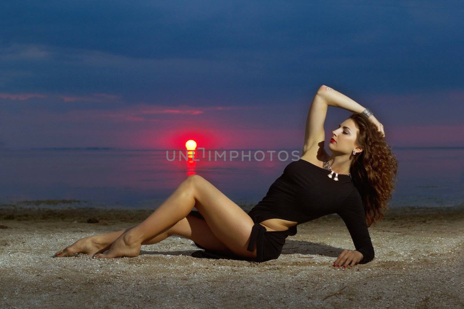 Attractive young woman lying on the shore at sunset
