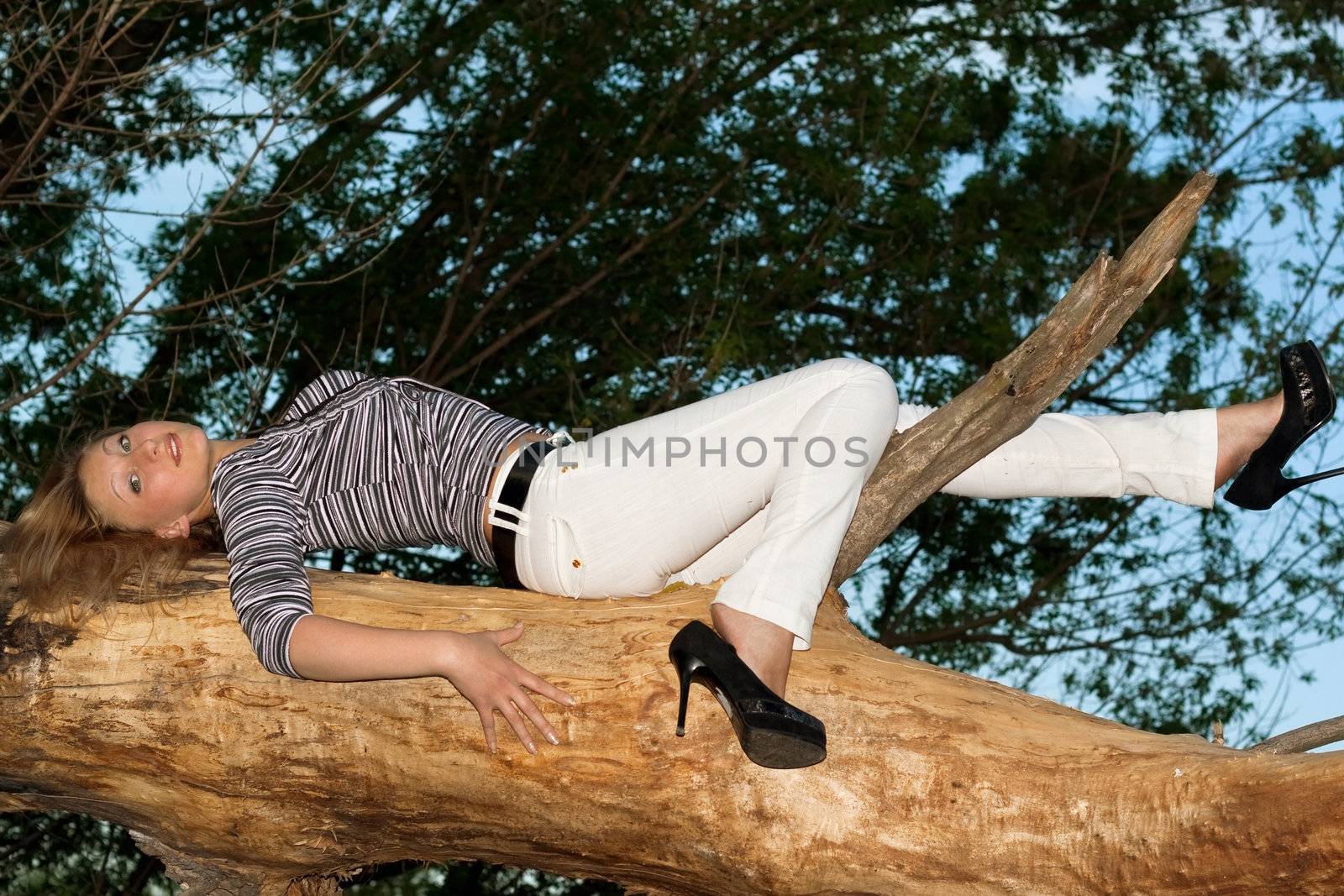 Smiling blonde lying on a tree branch