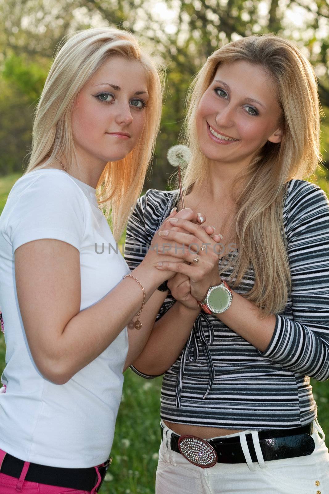 Two smiling young blonde with a dandelion