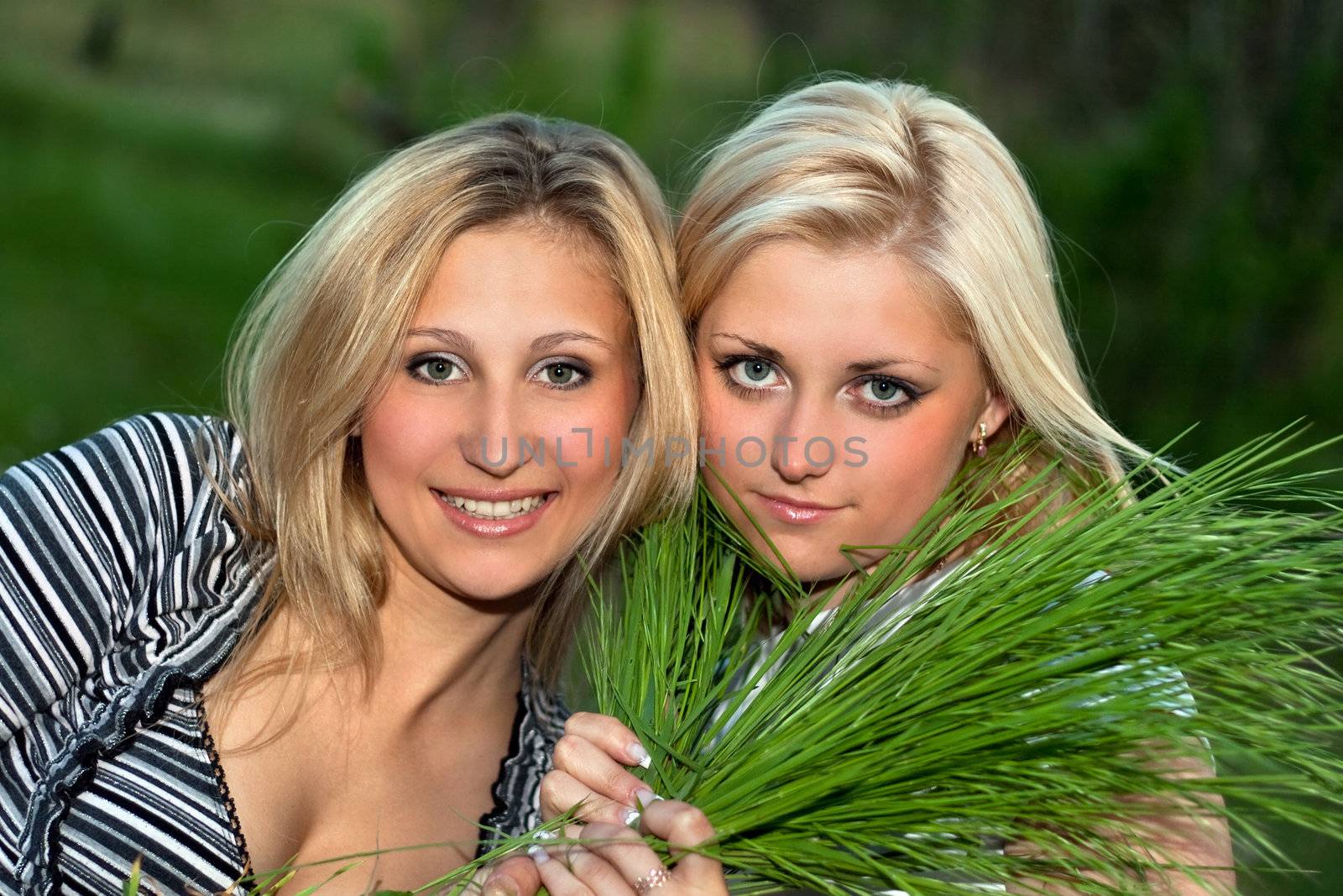 Two young blonde with green grass in their hands