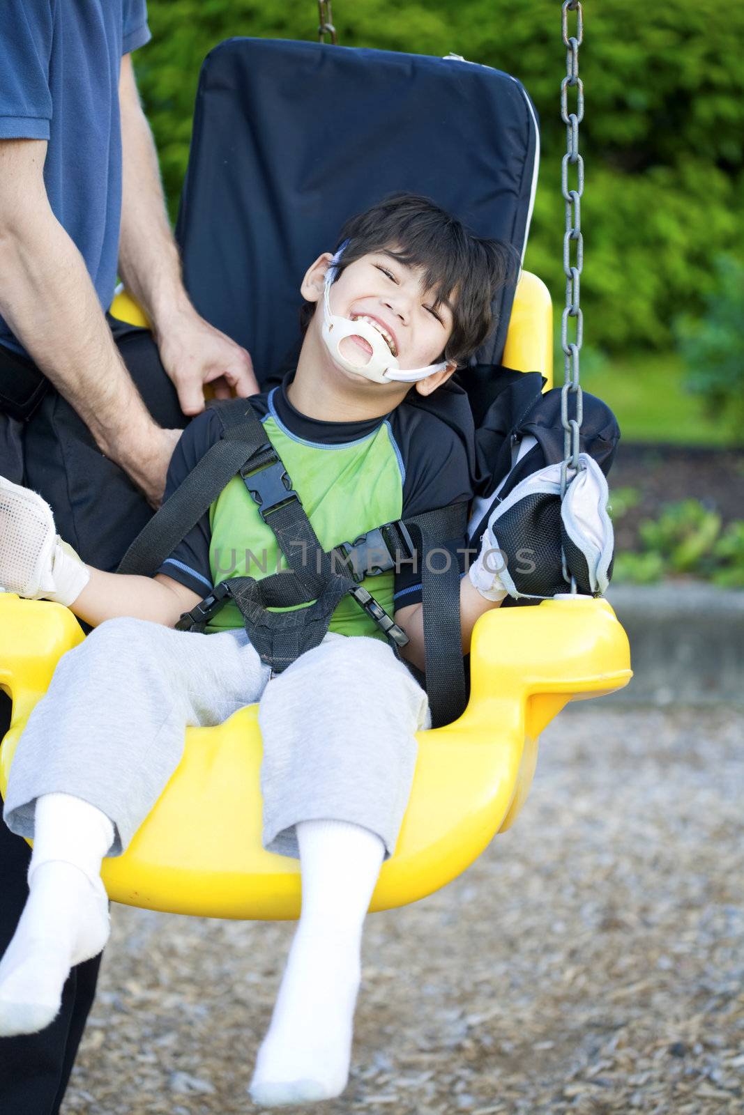 Disabled five year old boy getting strapped  into handicap swing