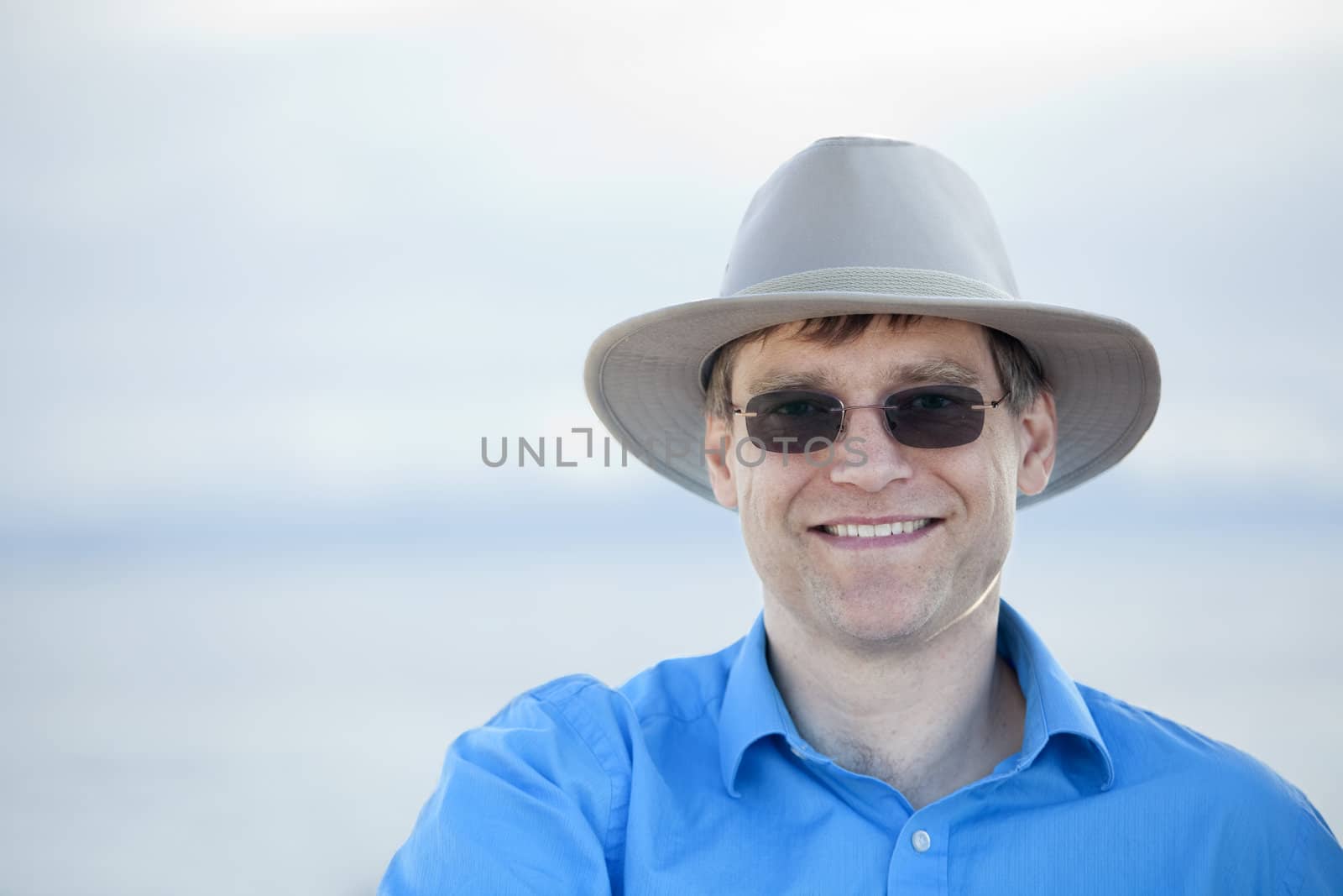 Handsome man wearing hat and sunglasses in early forties with blurred water background