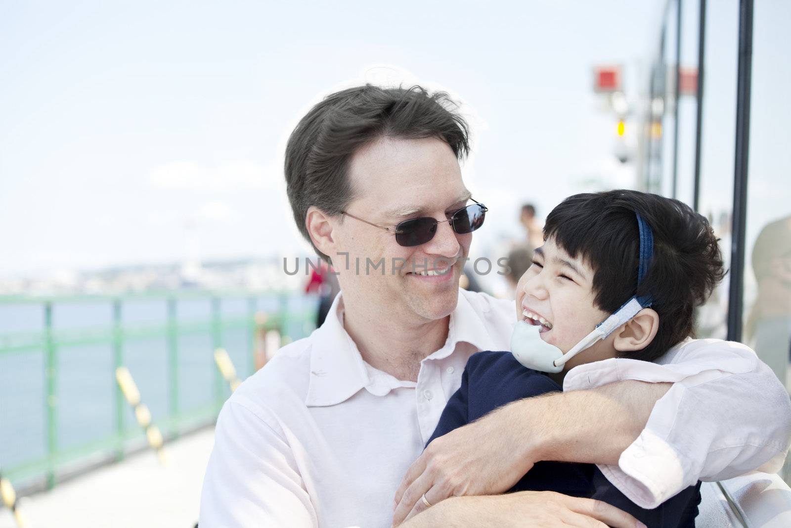 Father hugging disabled son as they ride a ferry boat by jarenwicklund