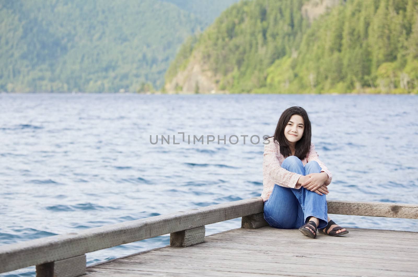 Young biracial teen girl sitting quietly on lake pier, relaxing