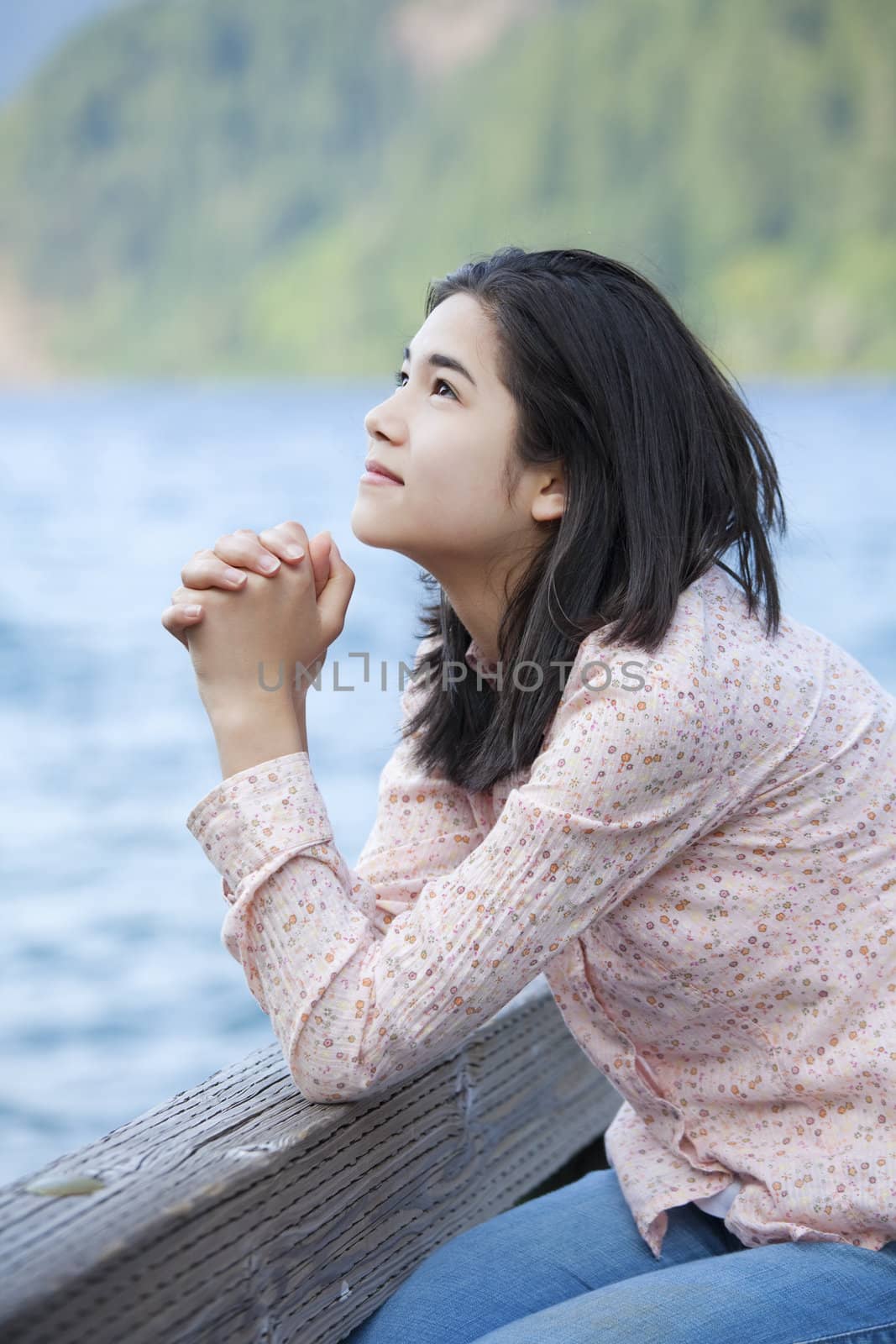 Young teen girl sitting quietly on lake pier, praying