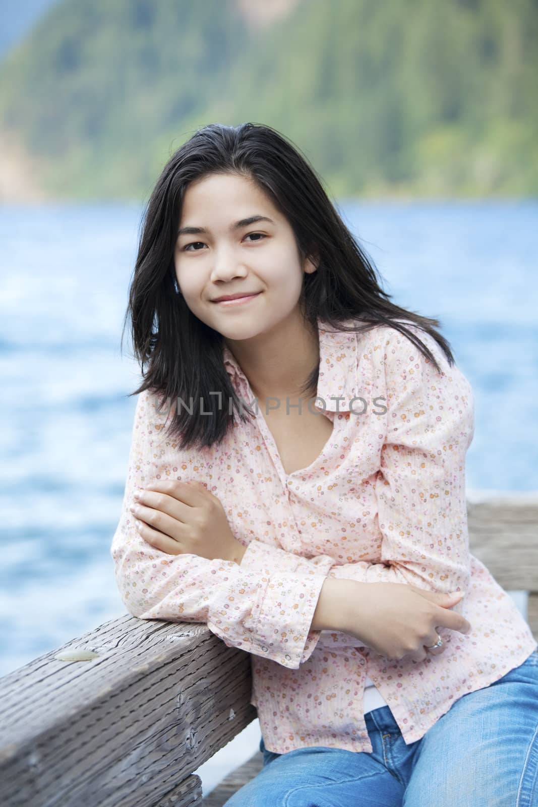 Young biracial teen girl sitting quietly on lake pier, relaxing