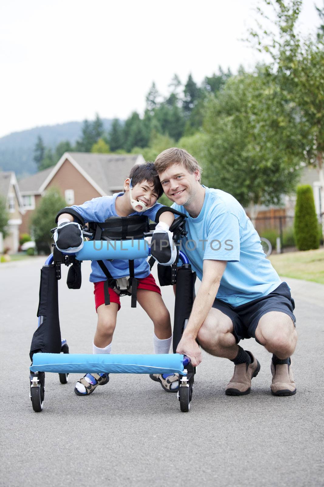 Father kneeling next to disabled son standing in walker