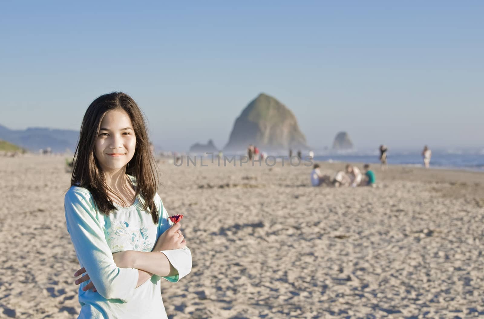 Beautiful preteen girl smiling on beach with Haystack Rock of Cannon Beach, OR in background