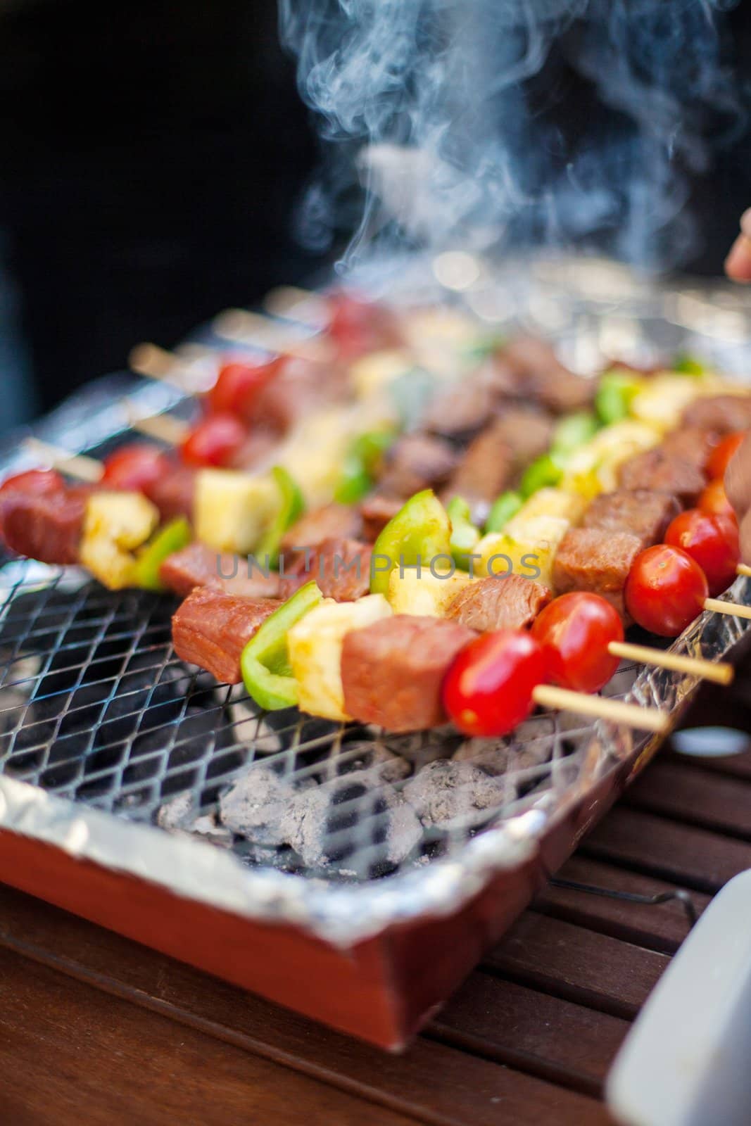 Thai style BBQ beef and vegetables on skewer grilling on a plate in outdoor cooking area.