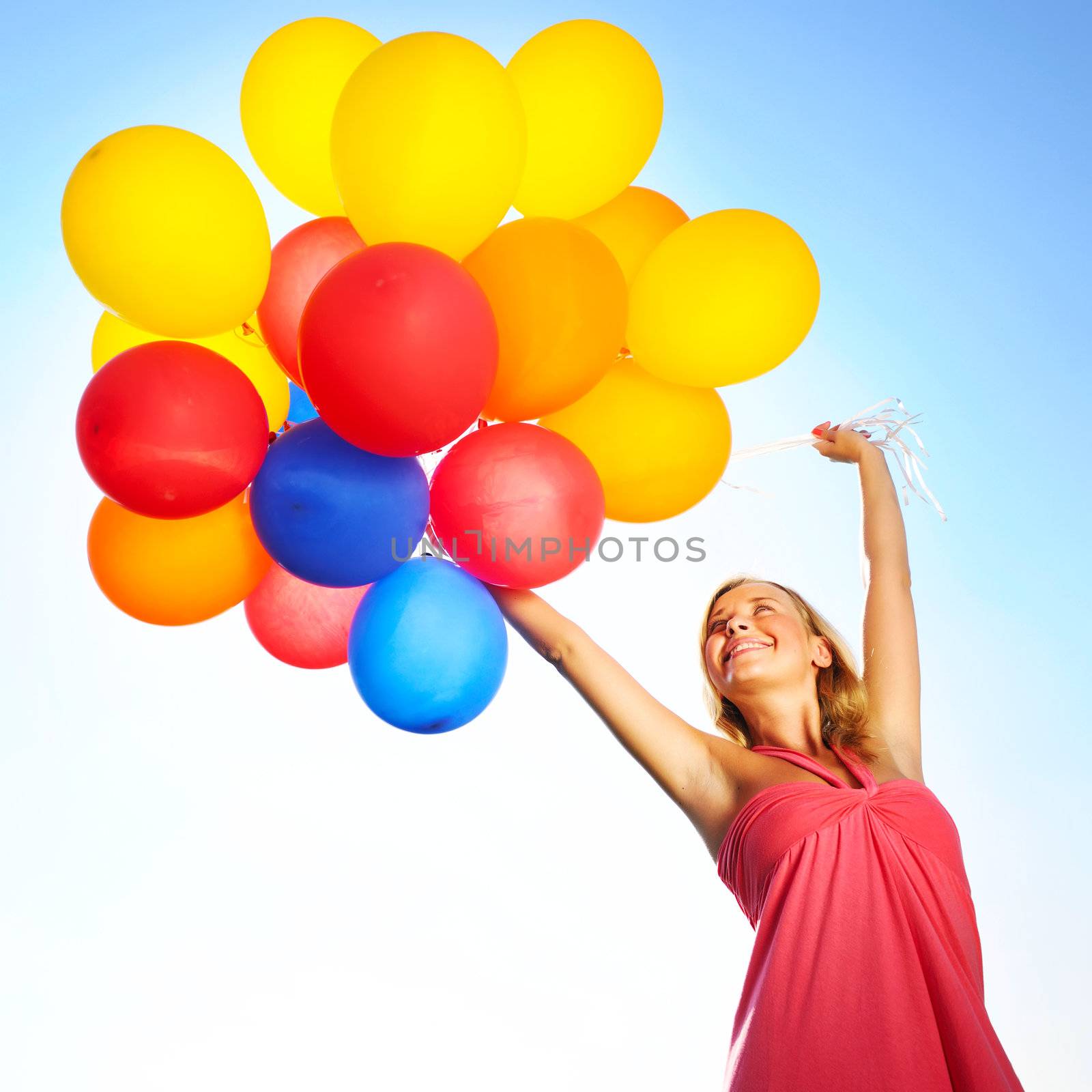 Woman holding balloons against sun and sky