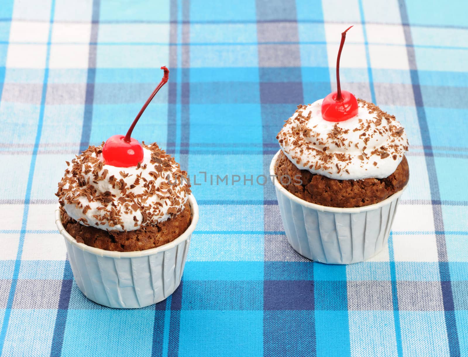 Cupcakes with whipped cream and cherry on a cloth