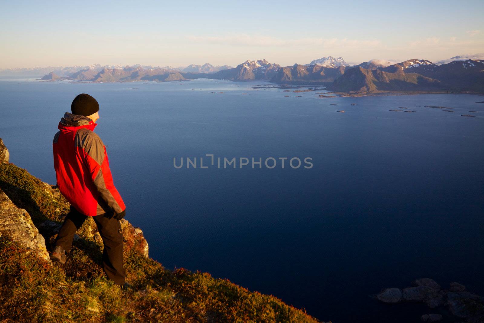 Young man on the top of mountain Festvagtinden with picturesque scenery of chain of Lofoten islands, Norway
