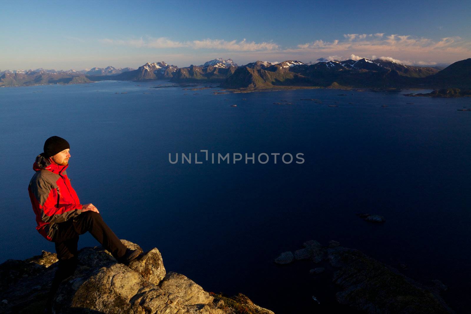 Active young man standing on the top of mountain Festvagtinden with breathtaking scenery of Lofoten islands, Norway