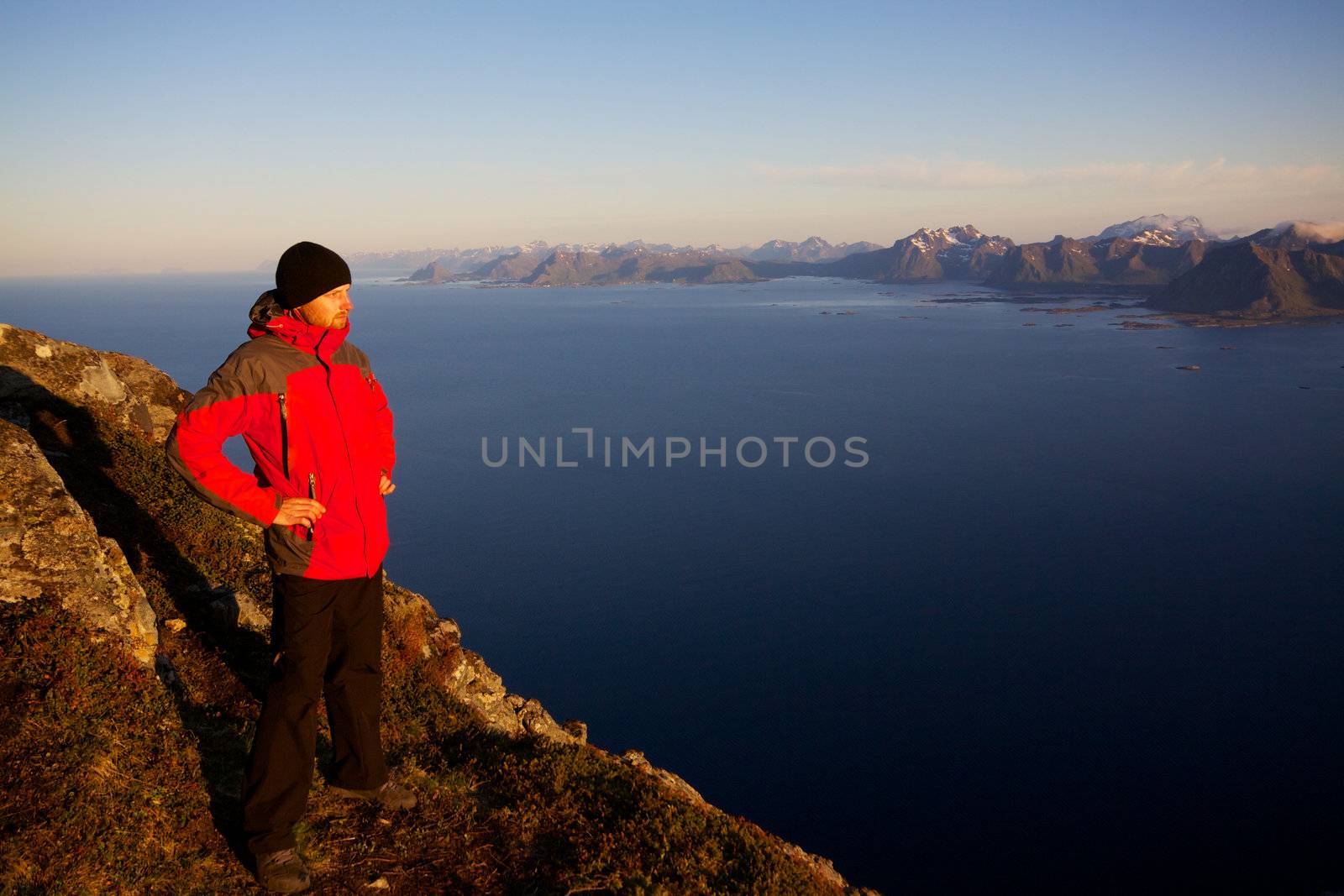 Young man standing on the top of mountain Festvagtinden with picturesque scenery of Lofoten islands, Norway