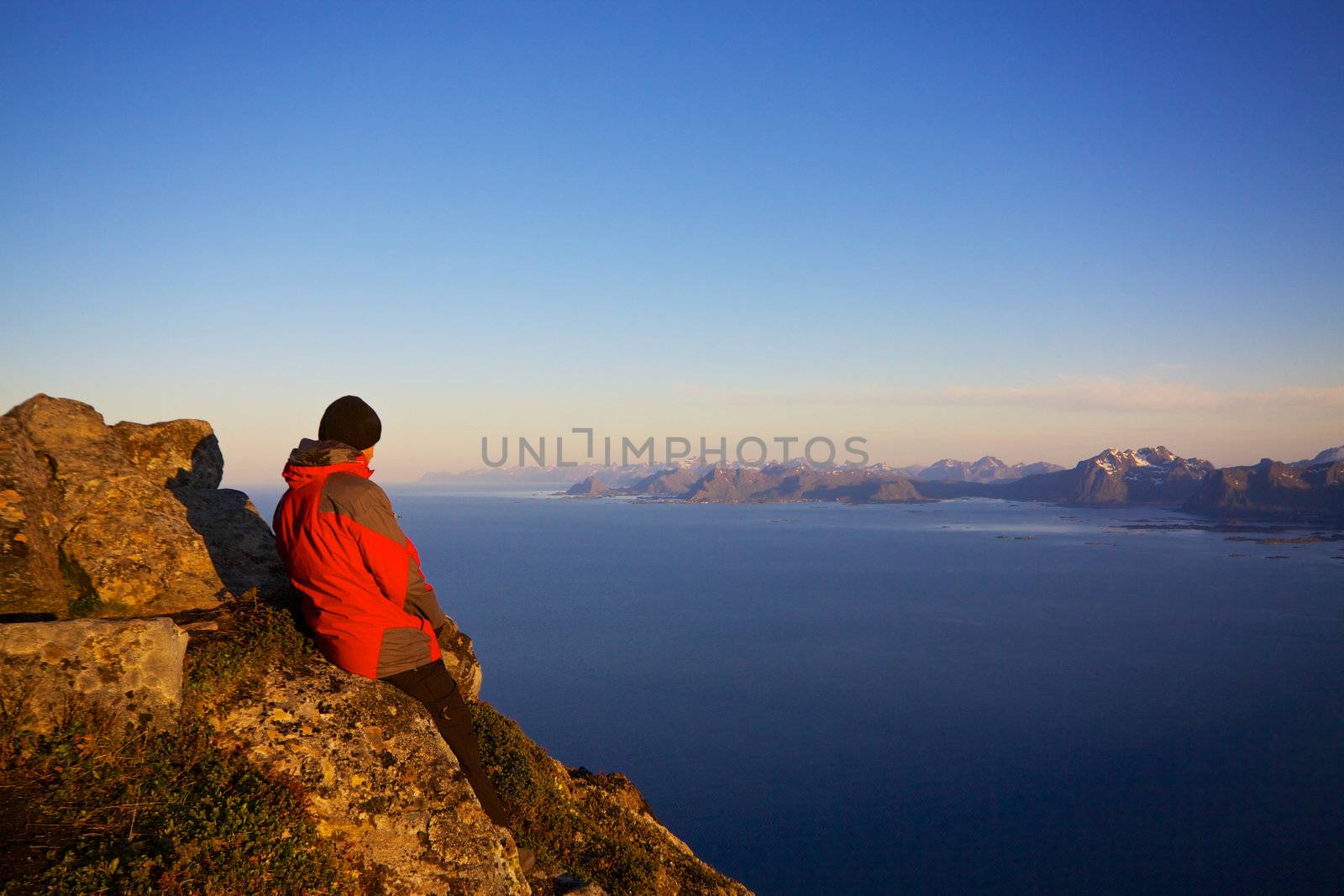 Young man enjoying scenic view of Lofoten islands in Norway from the summit of Festvagtinden, popular rock for climbers