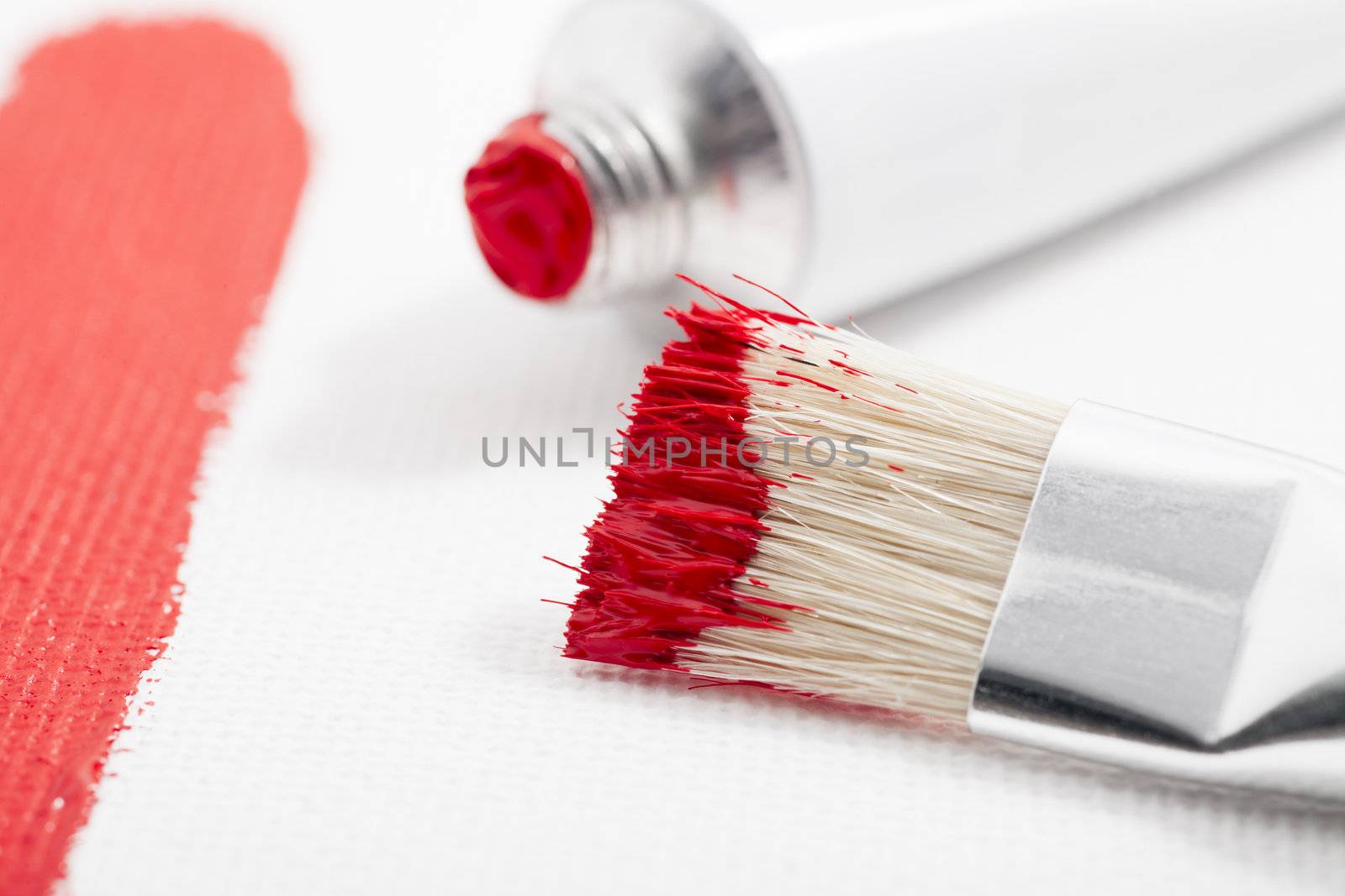 Red paint on paint brush with tube of acrylic paint and paint stroke on canvas