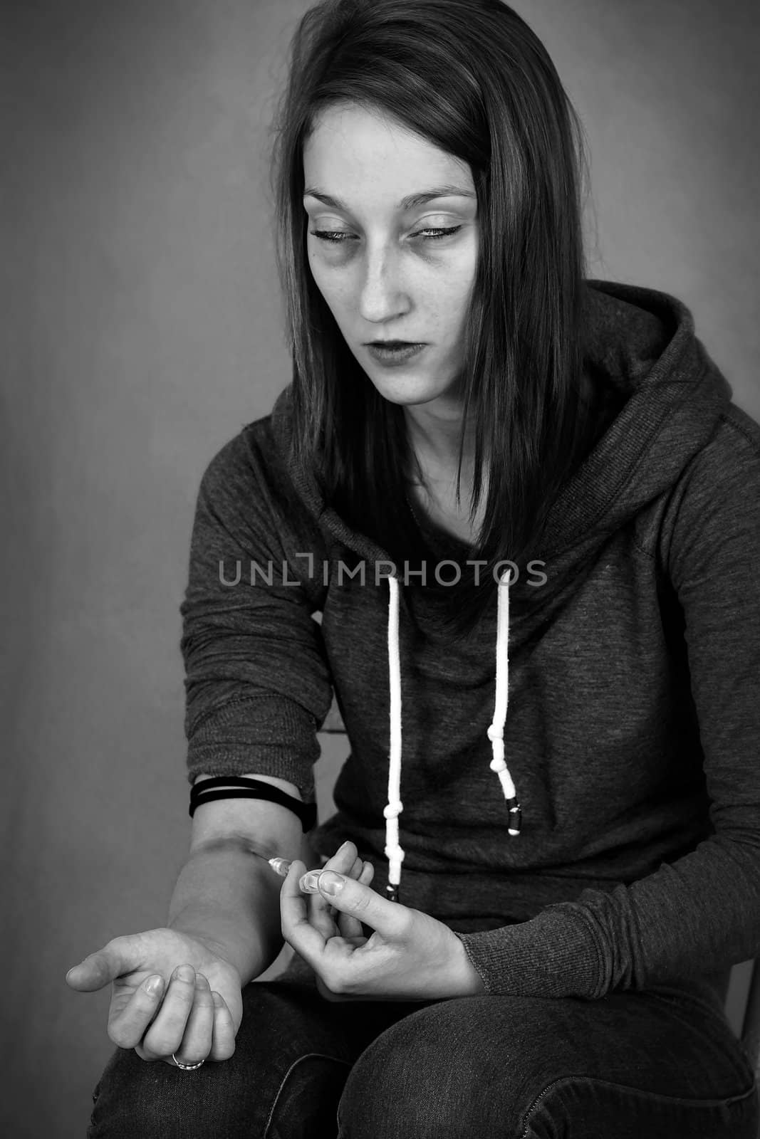 Dramatic black and white portrait of a young woman junkie, getting high injecting drugs, like heroin, with syringe in her arm; great for substance abuse and narcotics related social issues.