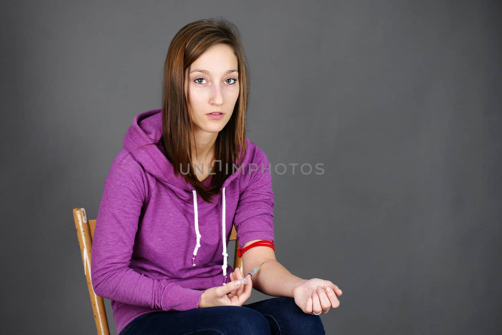 Young woman junkie, getting high injecting drugs, like heroin, with syringe in her arm; great for substance abuse and narcotics related social issues.