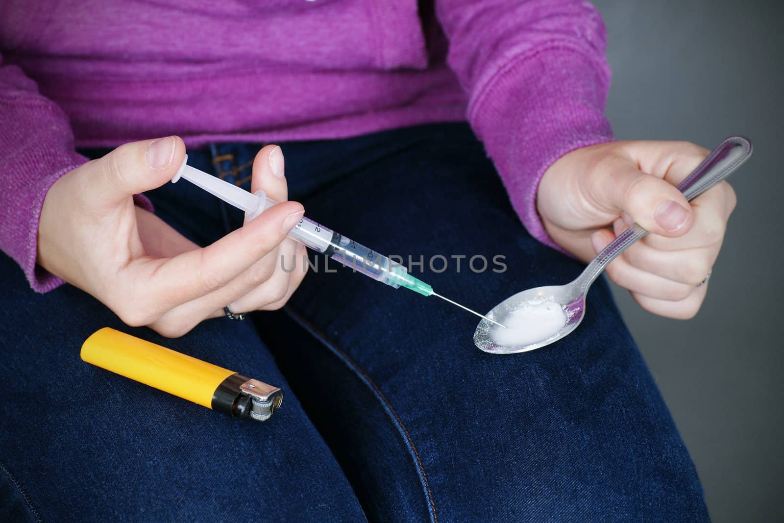 Drug paraphernalia: young woman junkie preparing heroin or the likes for injection with the syringe. 