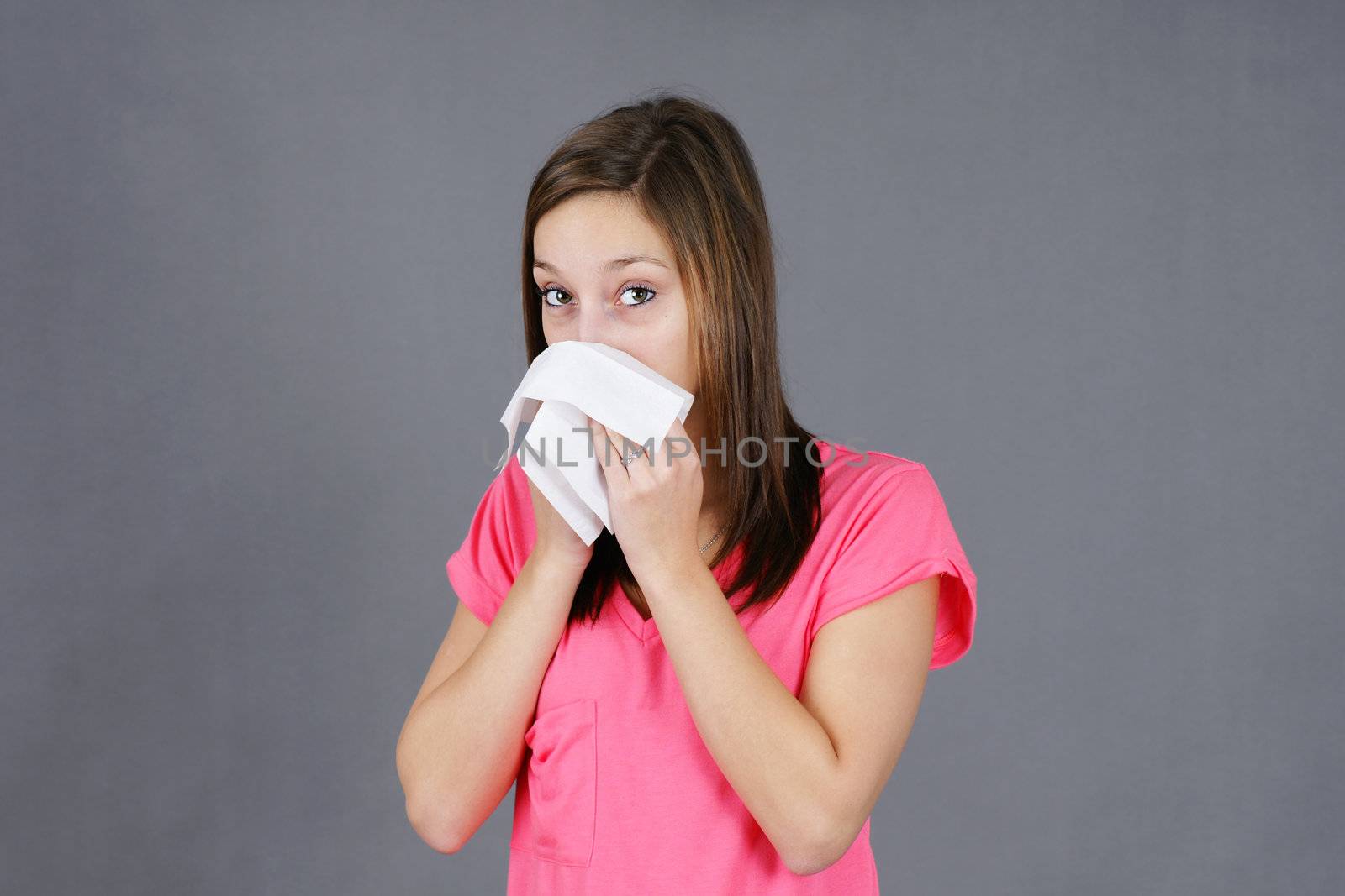 Young woman blowing her nose in a tissue, sick from a cold or flu virus, could be sad or depressed, great for health issues.