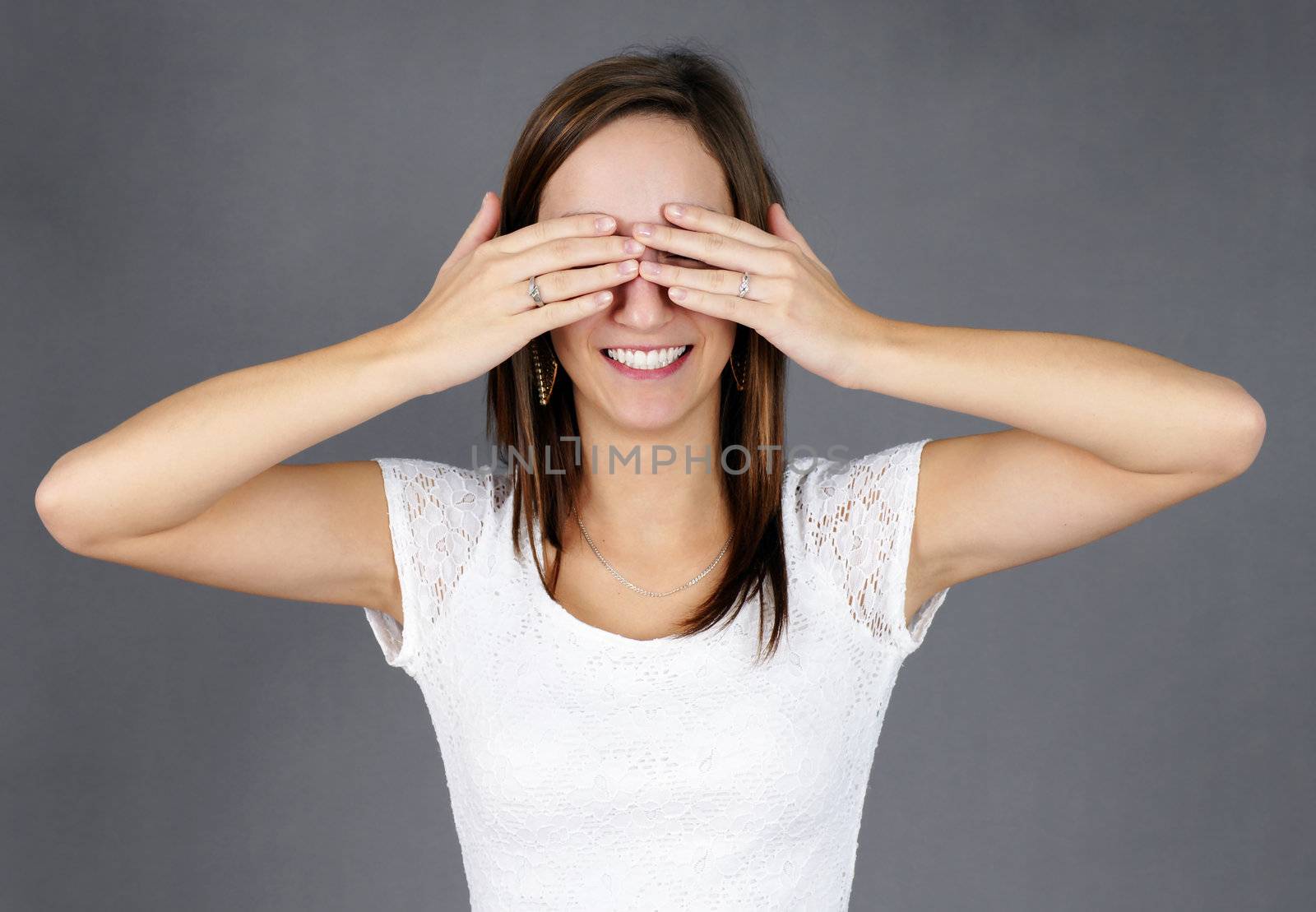 Dressed up young woman with hands on her eyes, smiling, waiting for her big surprise; can be used for wedding proposal, birthday party or others.