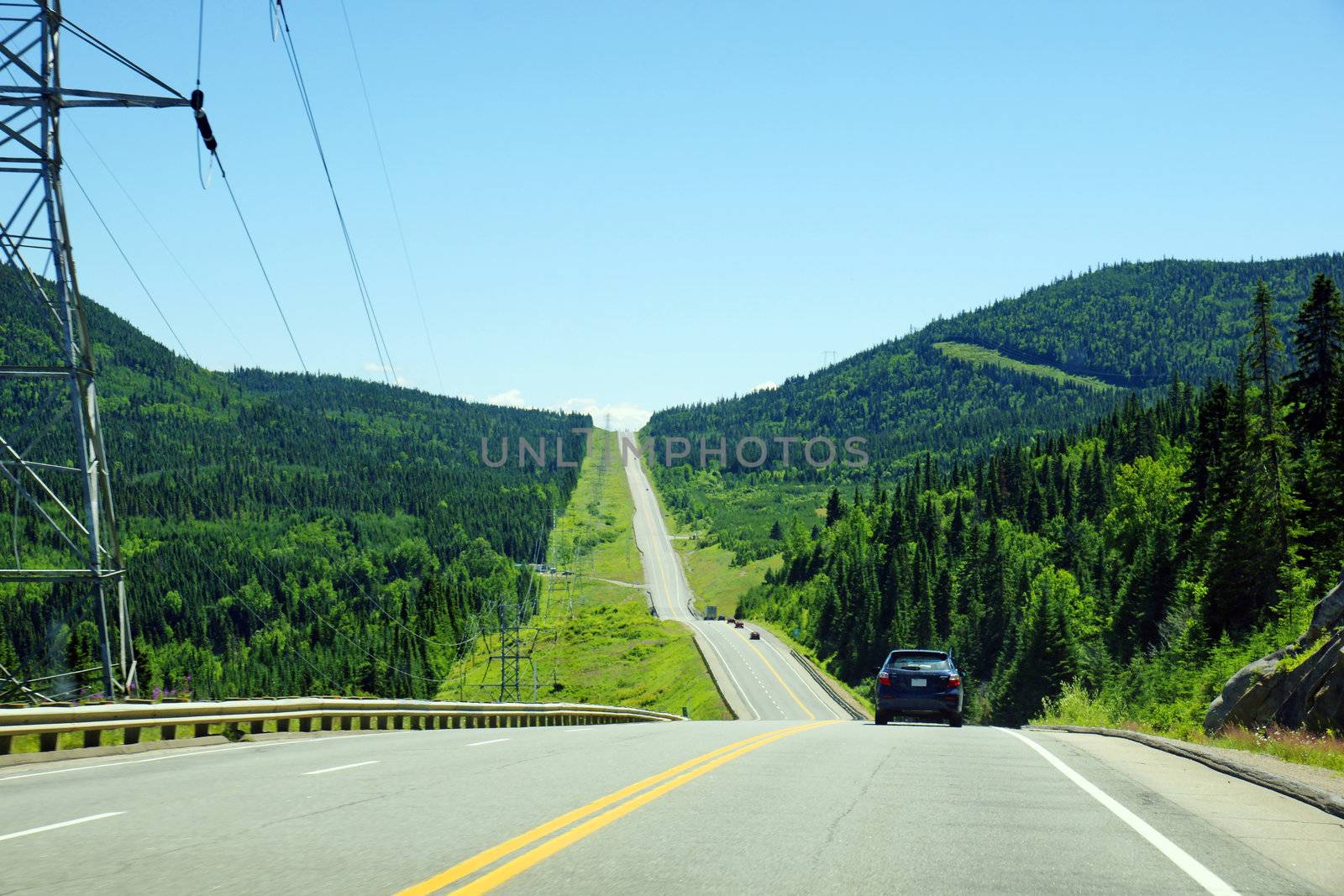 Mountain road in black spruce boreal forest of Canada with electric pilones close by, parc des laurentides, quebec.