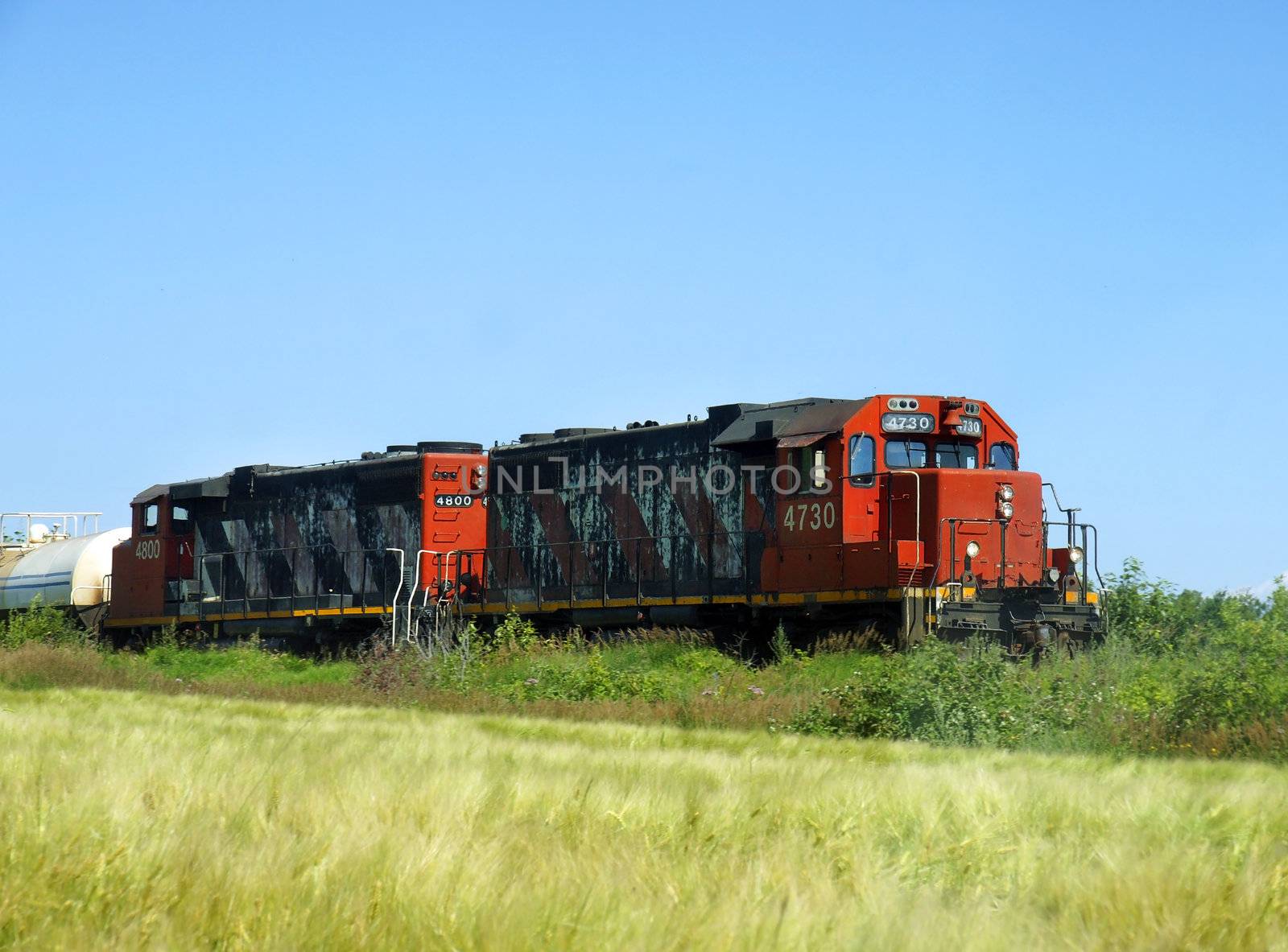 Two old freight or cargo locomotives going through farmland or prairies to deliver products and merchandises.