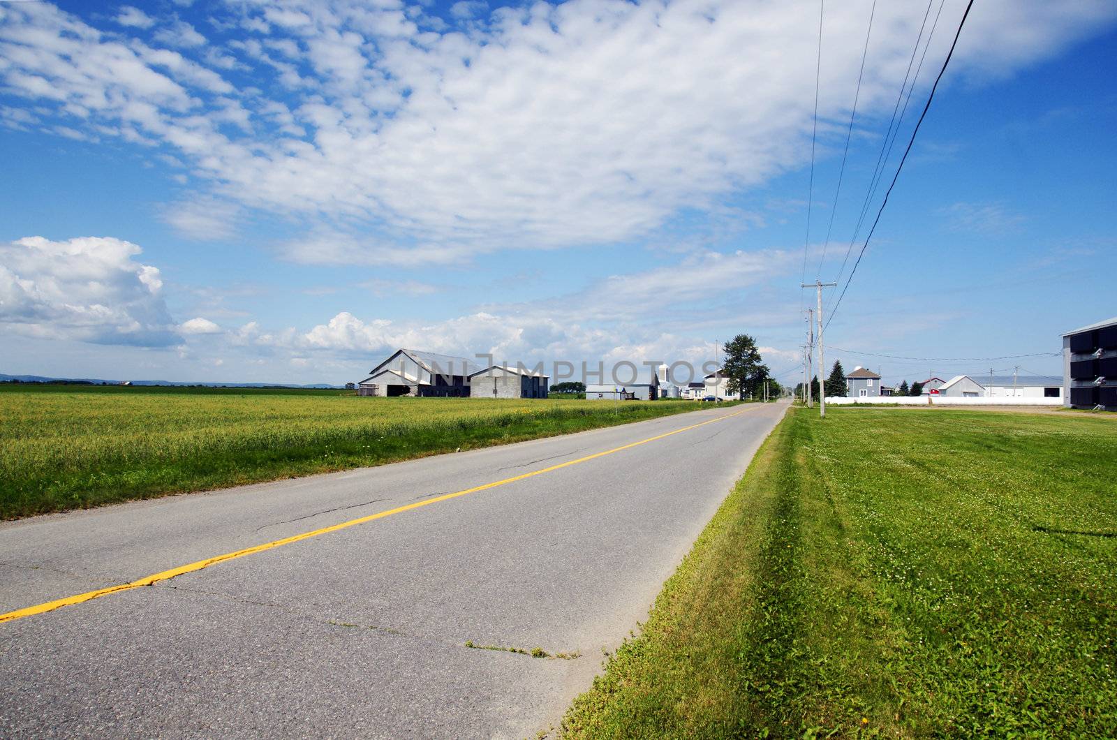 Perspective shot of the country side with a rural road in Quebec, Canada, with fields and farms, barn, hay bales and chicken coop.