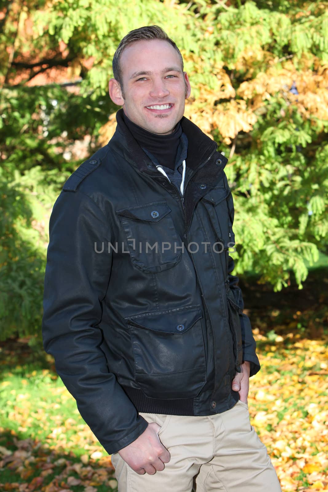 Handsome trendy young man with a cheerful smile standing alone in autumn woodland