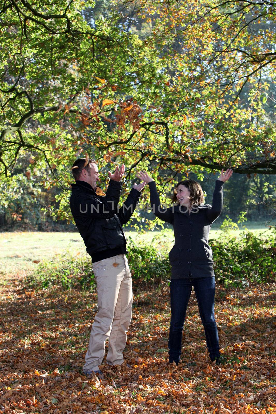 Young couple enjoying the autumn forest standing holding the branch of a tree collecting colourful autumn leaves
