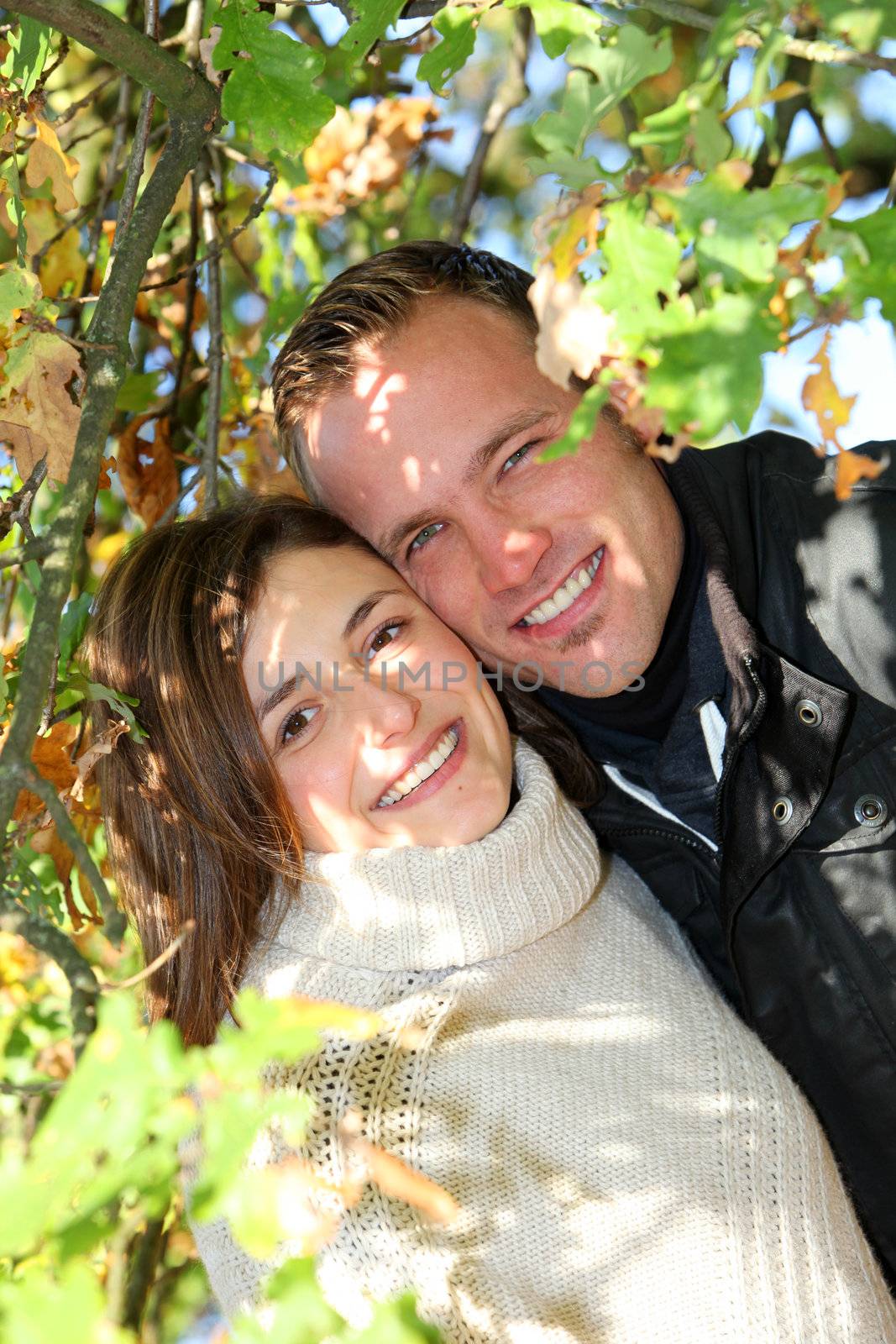 Portrait of an attractive loving young couple standing framed by autumn foliage smiling happily at the camera Portrait of a happy smiling attractive loving young couple standing framed by autumn foliage