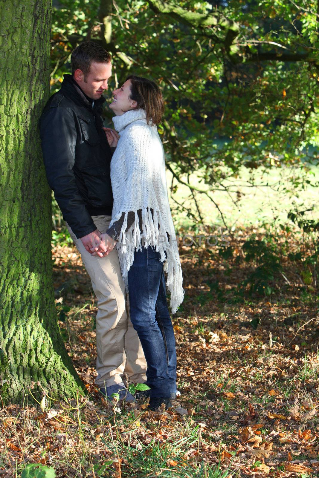 Loving young couple standing under a large tree in the forest holding hands and looking into each others eyes poised to kiss