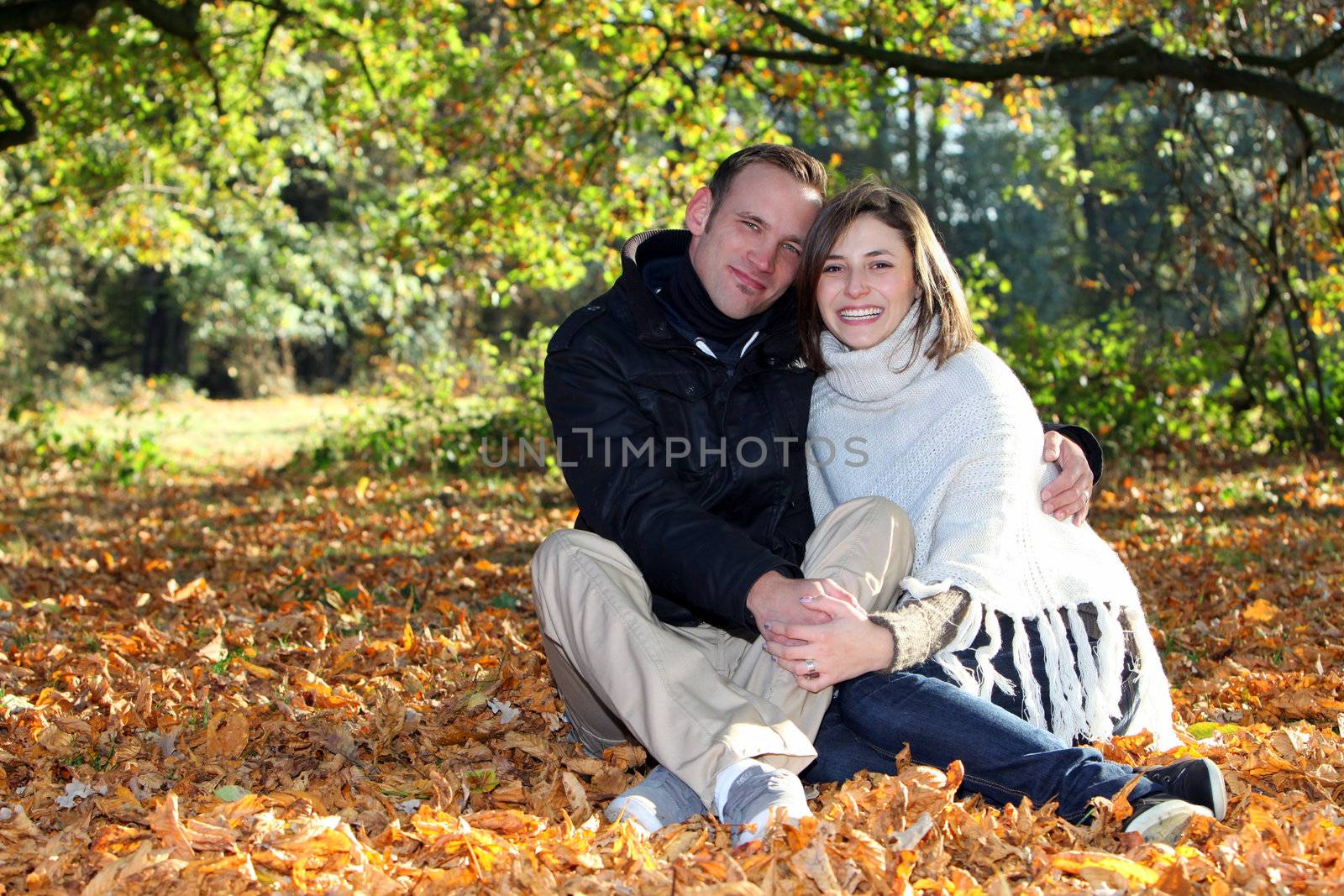 Happy young couple in love sitting in a close embrace amonst autumn leaves in the forest with copyspace