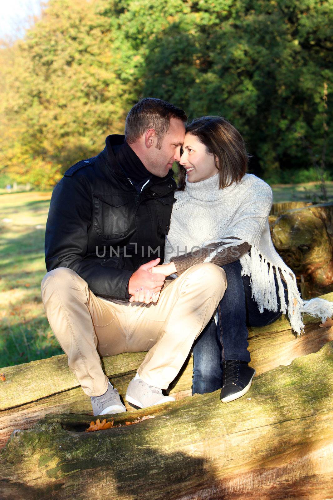 Young couple in love sitting on a fallen log in the countryside looking into each others eyes with tenderness and devotion
