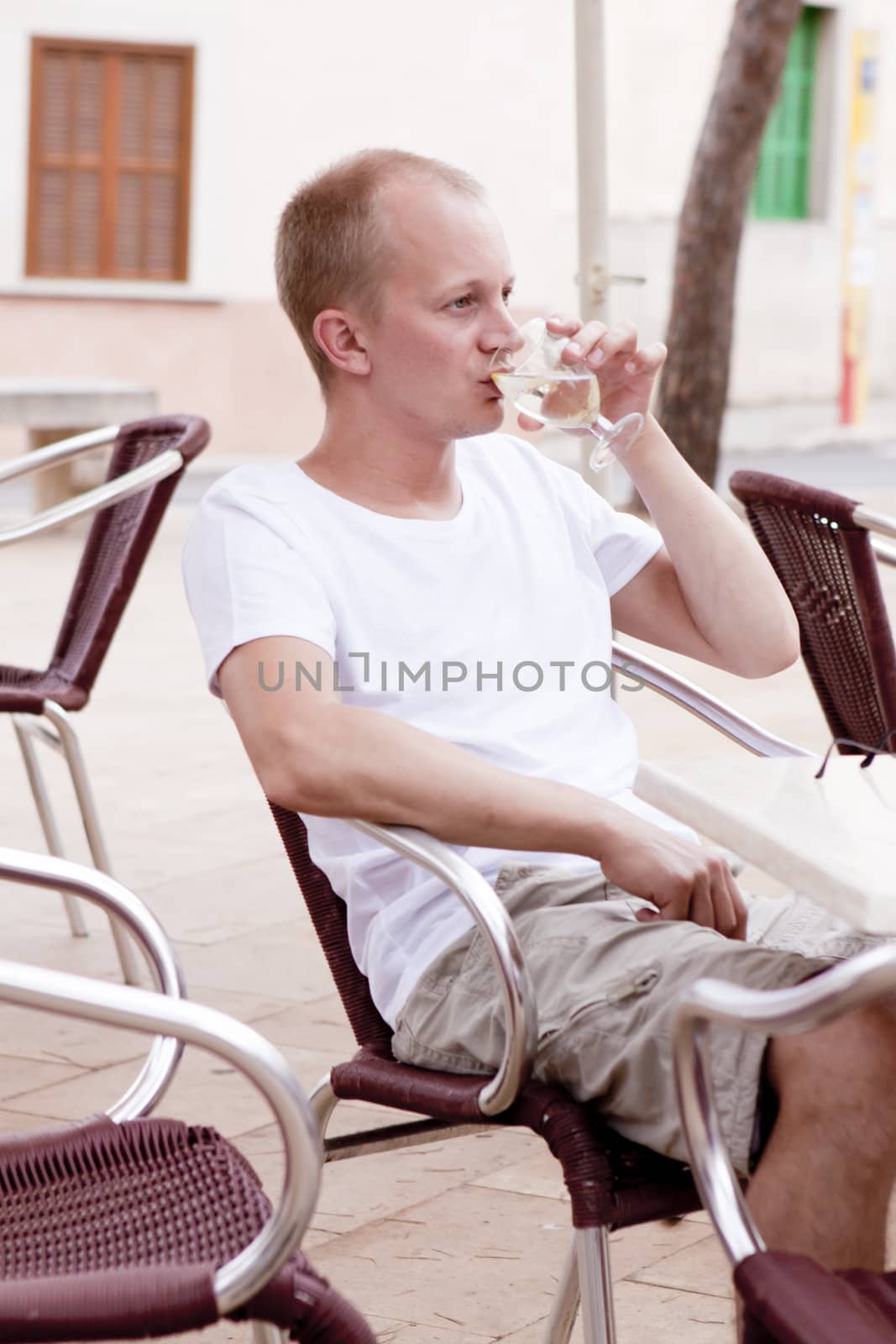 young man sitting outdoor in a cafe in summer drinking water