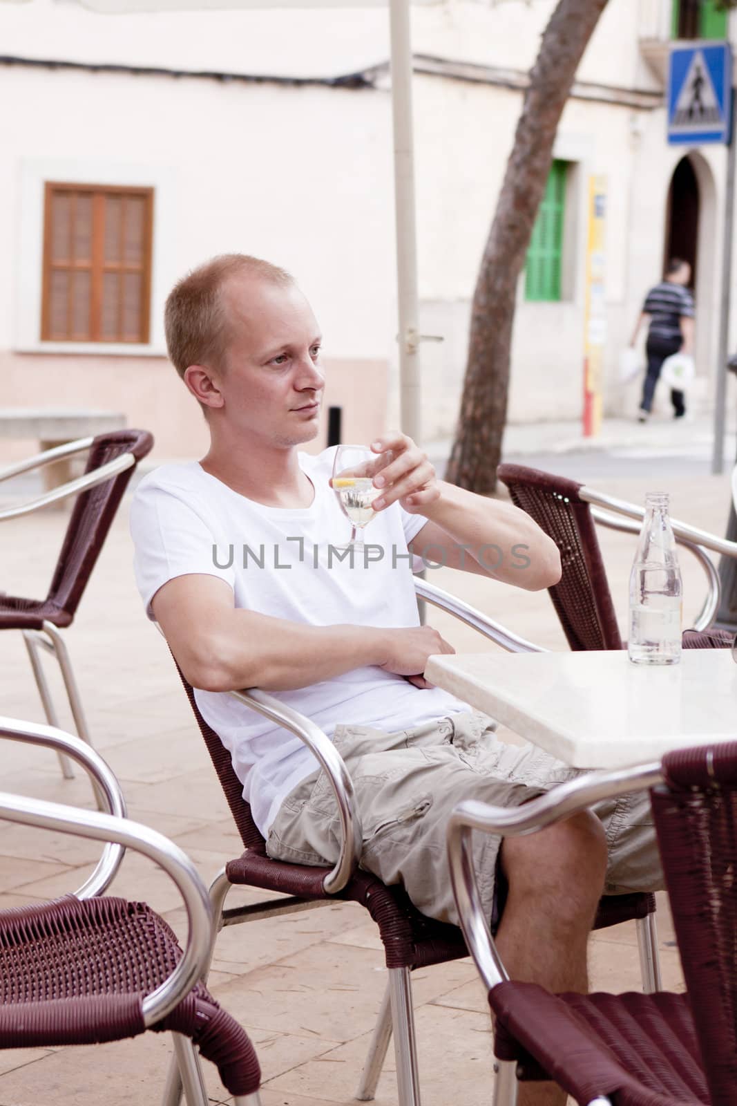 young man sitting outdoor in a cafe in summer drinking water