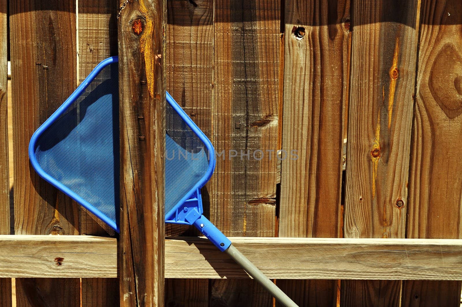 A backyard pool skimmer rests on a wooded fence.