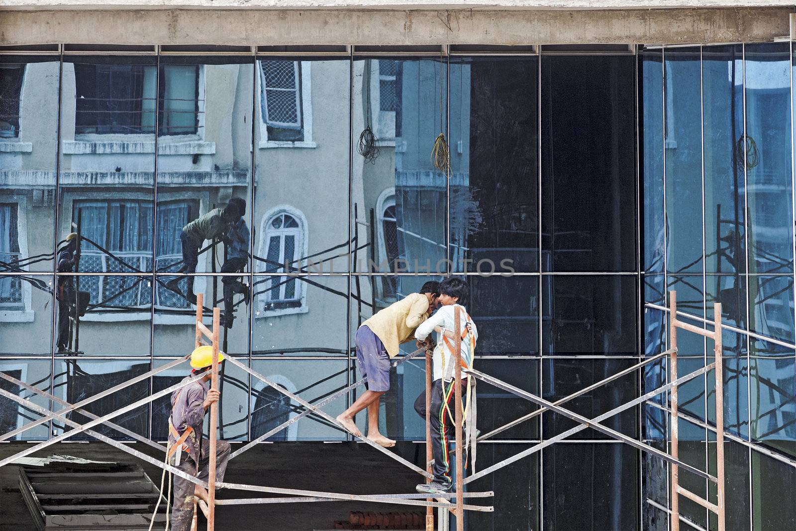 Builders on a scaffolding at work on a high rise block with the reflections showing on glass window surfaces
